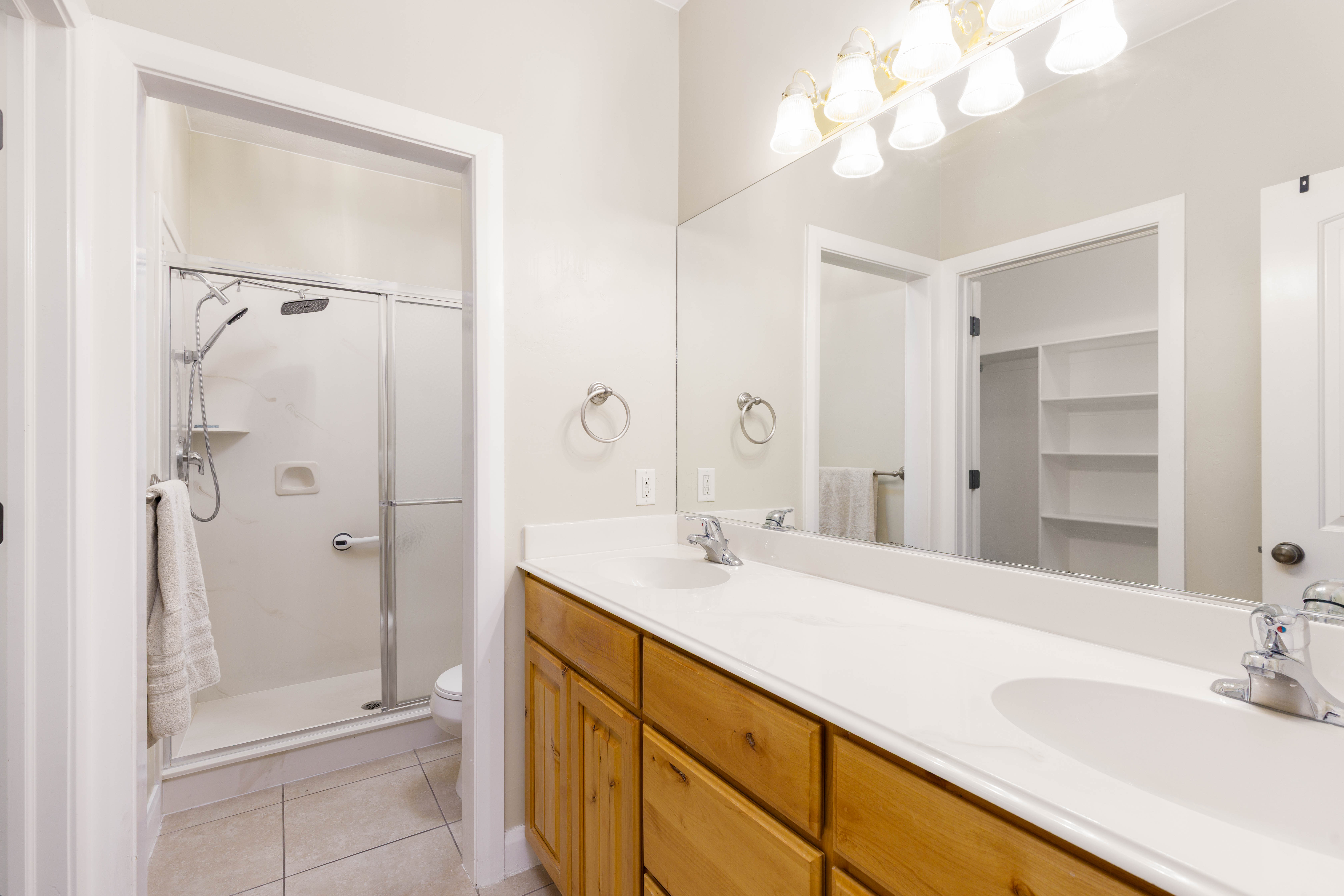 Bathroom featuring a dual-sink vanity with wood cabinetry, a large frameless mirror, and a multi-bulb light fixture