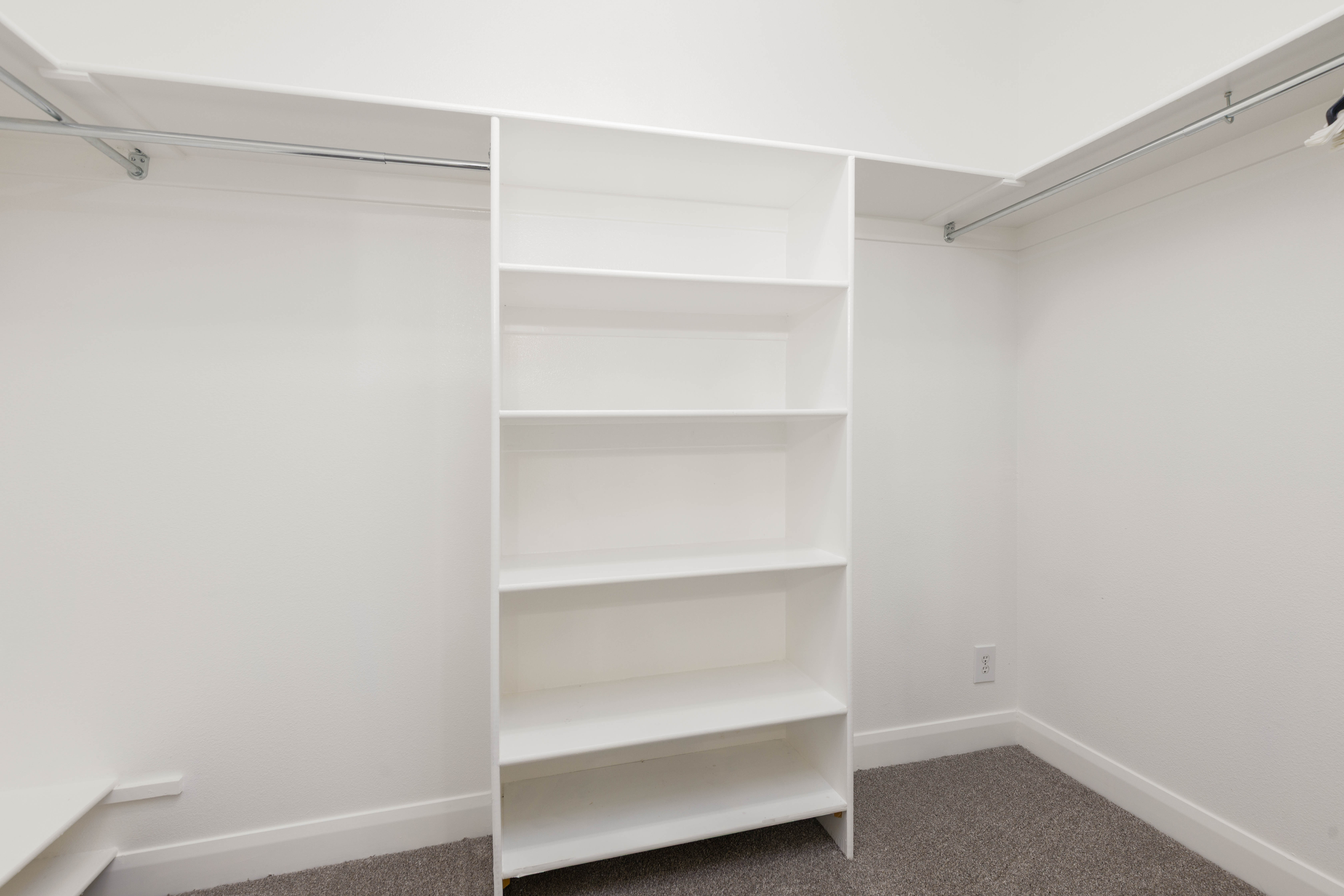 Walk-in closet featuring white built-in shelving, chrome hanging rods, white walls, and gray carpet flooring