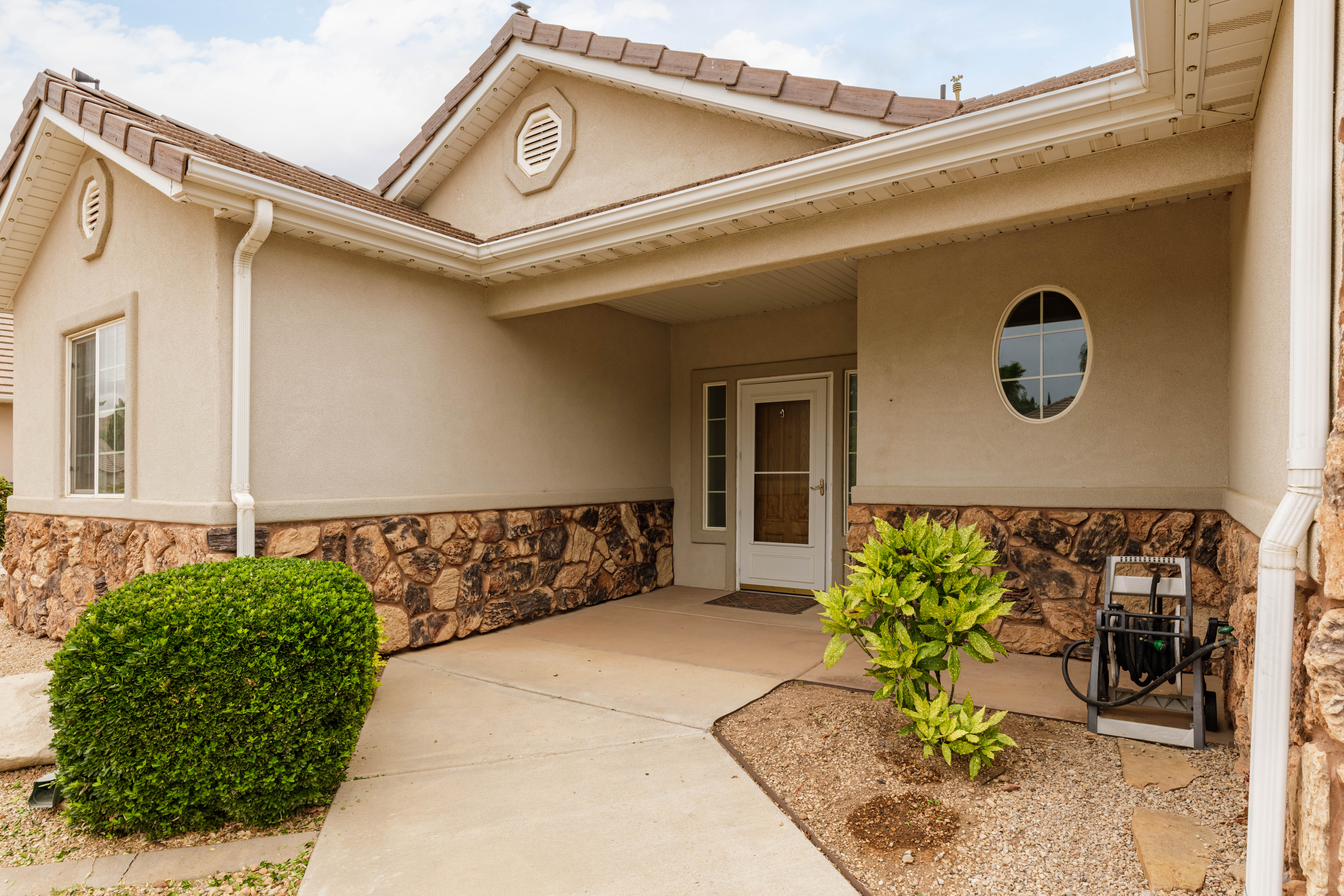 Stucco exterior featuring a stone accent foundation, a covered entry, and a decorative oval window
