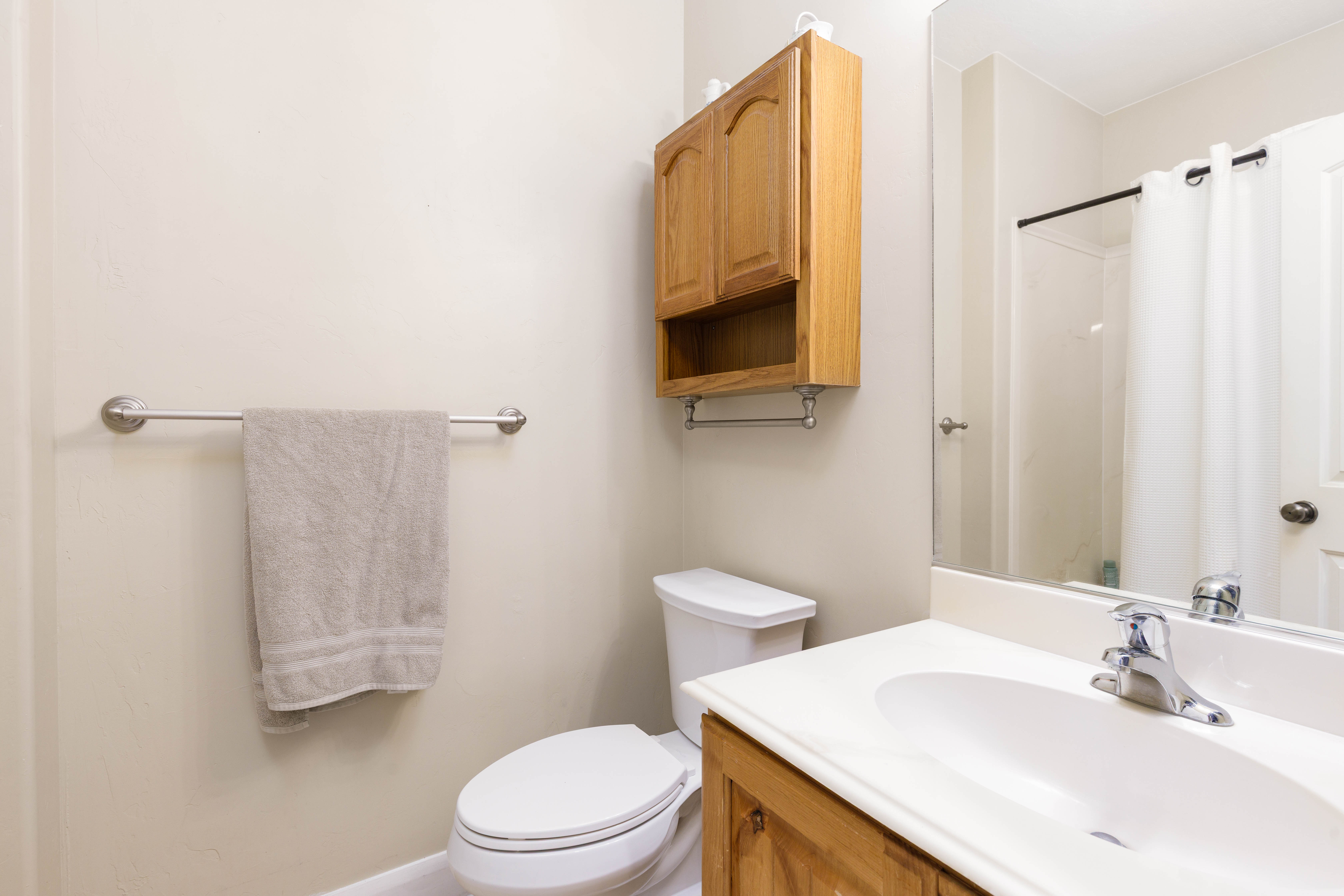 Bathroom featuring a single vanity with wood-finish cabinetry and white countertop, chrome faucet, wall-mounted mirror, and a white toilet
