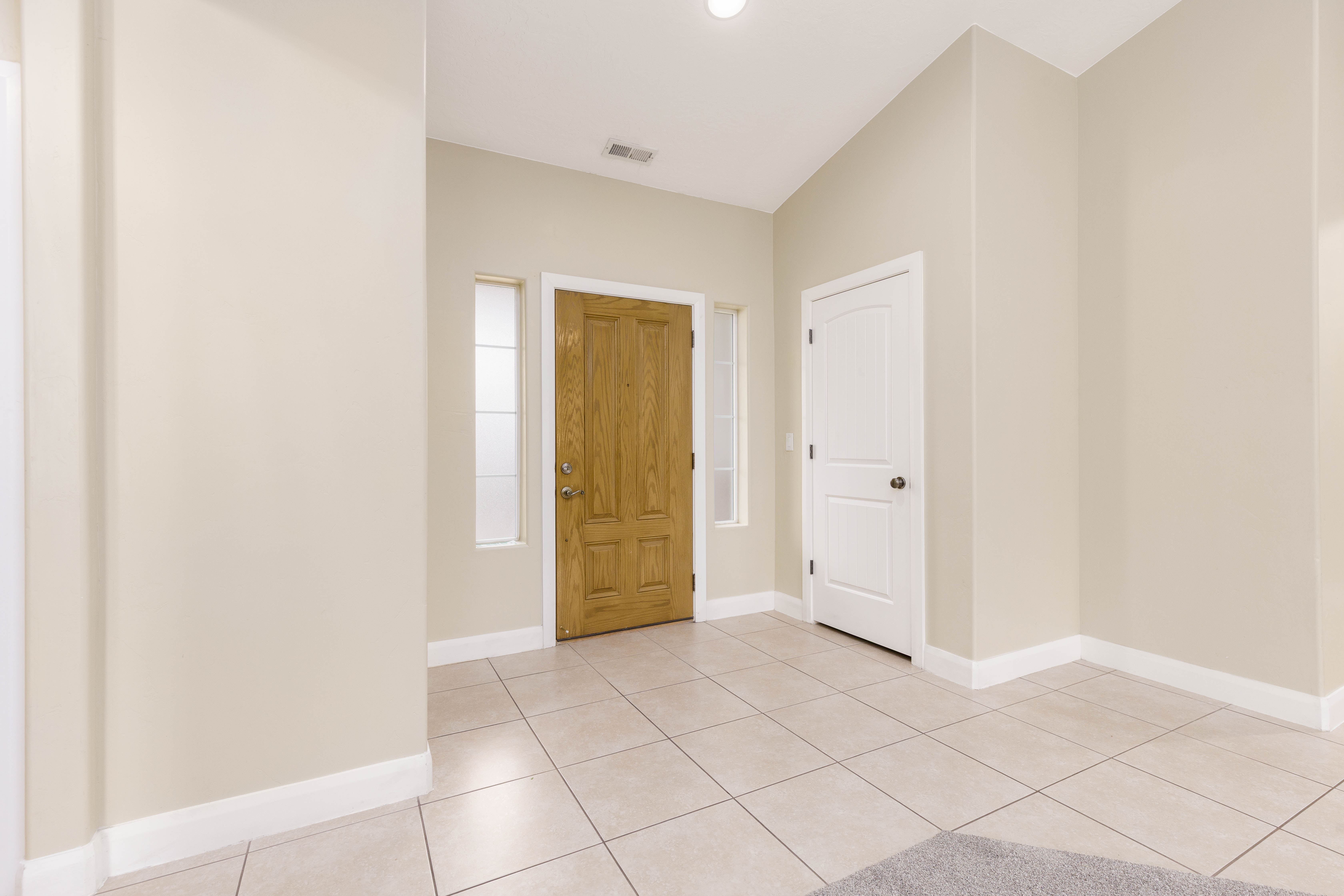 Entryway featuring a natural wood-finish front door with sidelights, neutral-toned walls, white trim, and light-colored tile flooring
