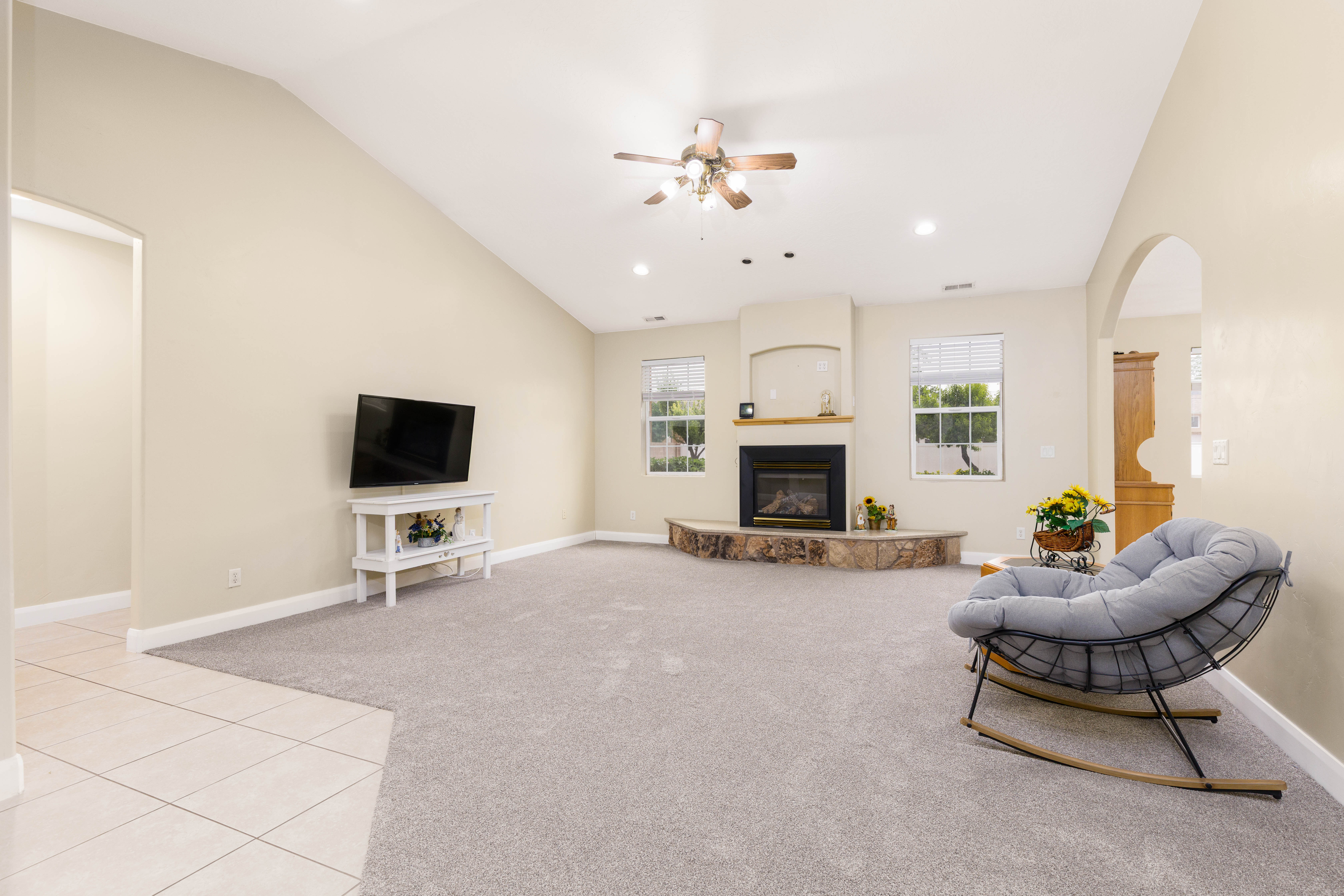 Spacious living area featuring vaulted ceilings, a fireplace with a wood mantle and stone hearth, recessed lighting, and ceiling fan