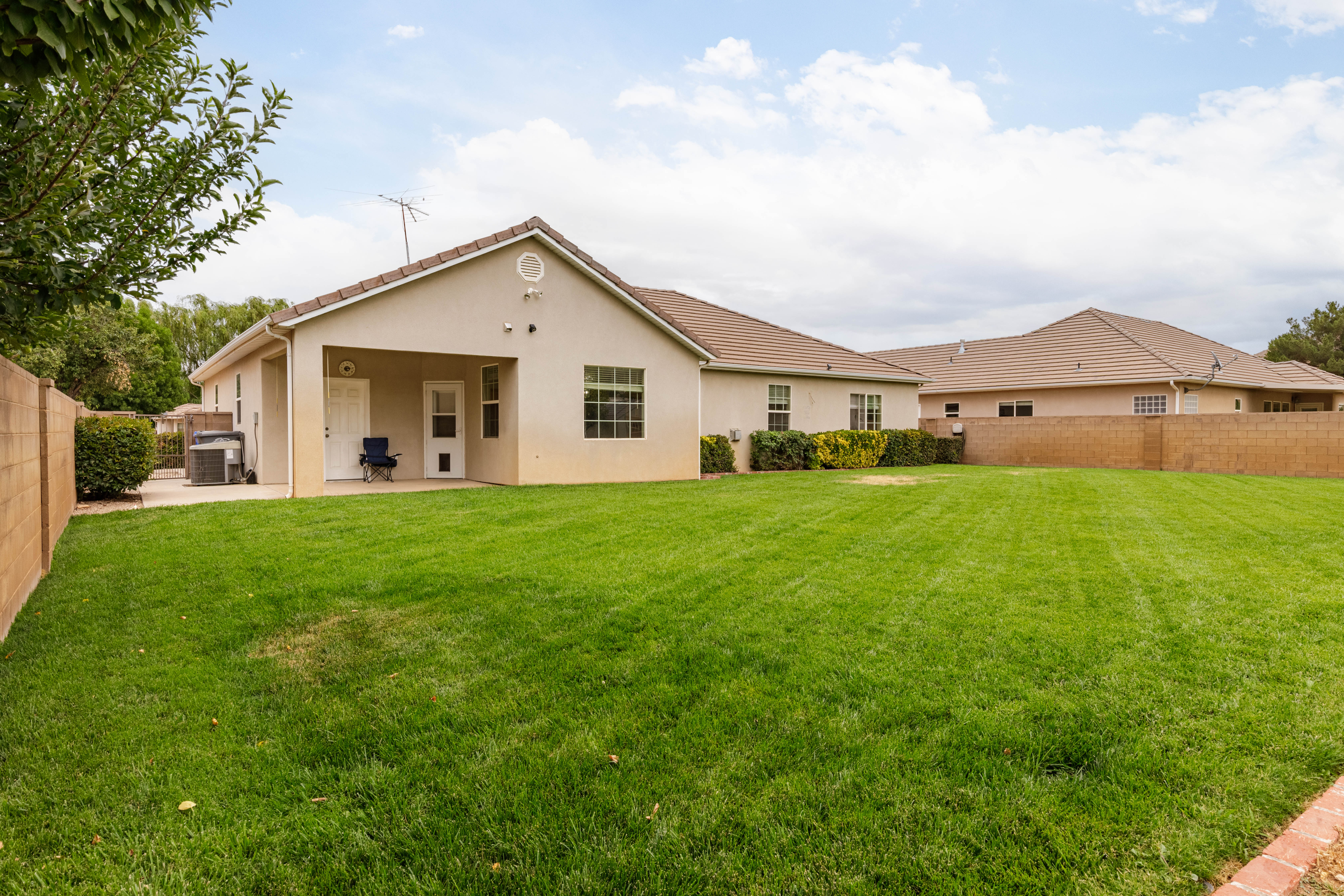 Expansive rear lawn area with a covered patio, stucco exterior, and tile roof