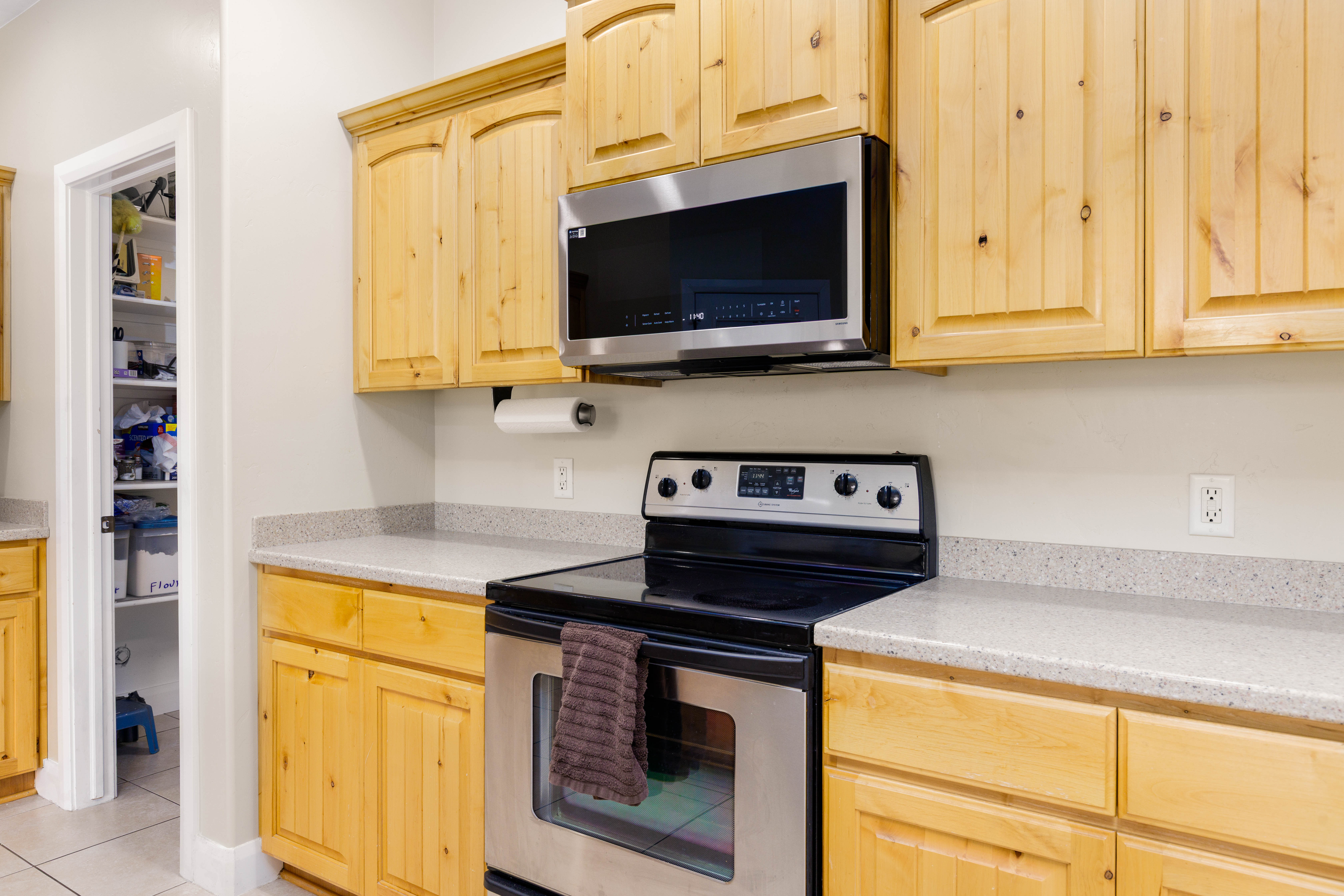 Kitchen featuring natural wood cabinetry, light-toned countertops, a stainless steel over-the-range microwave, and a black and stainless steel electric range