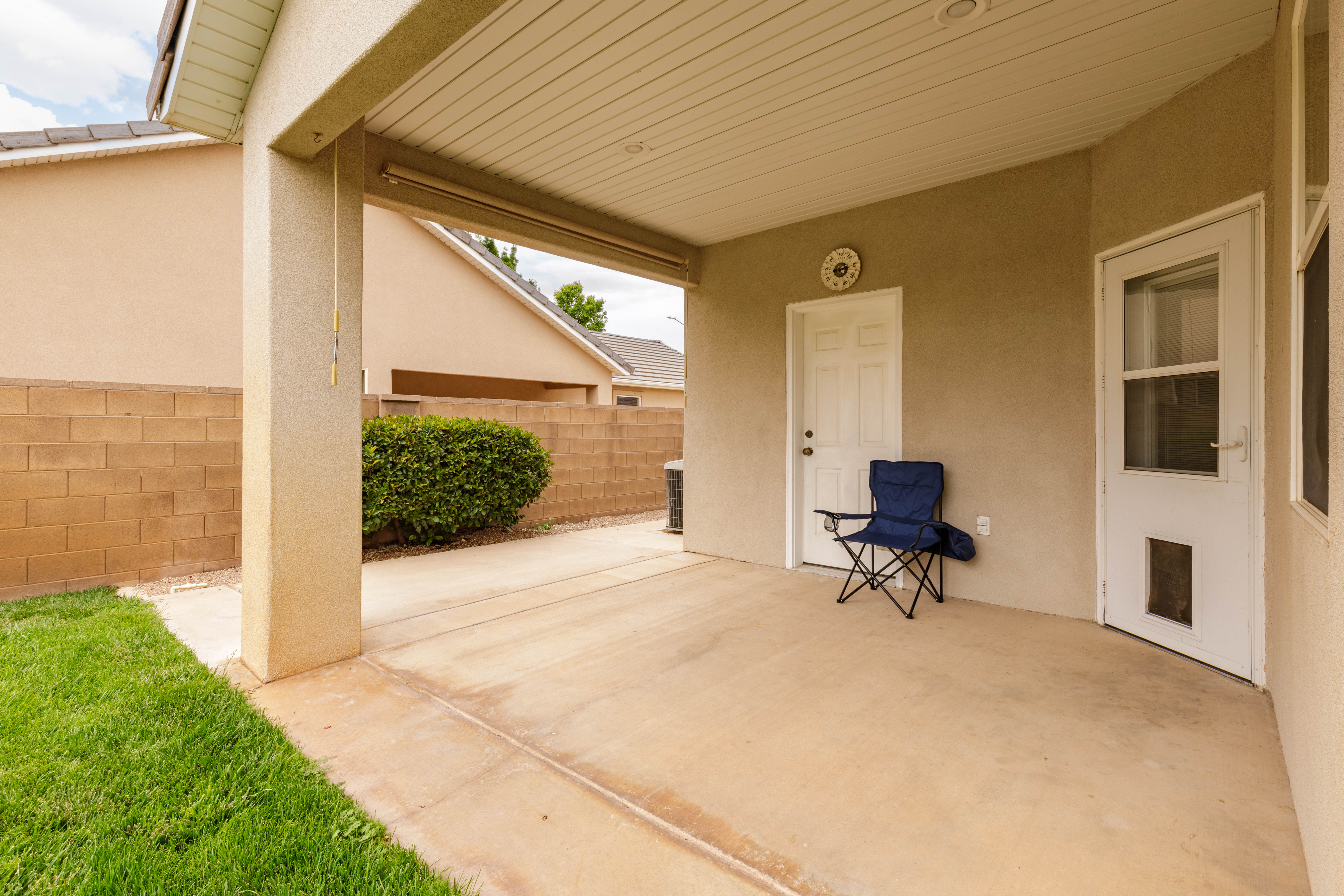 Covered patio area with concrete flooring, stucco wall, and a white exterior door
