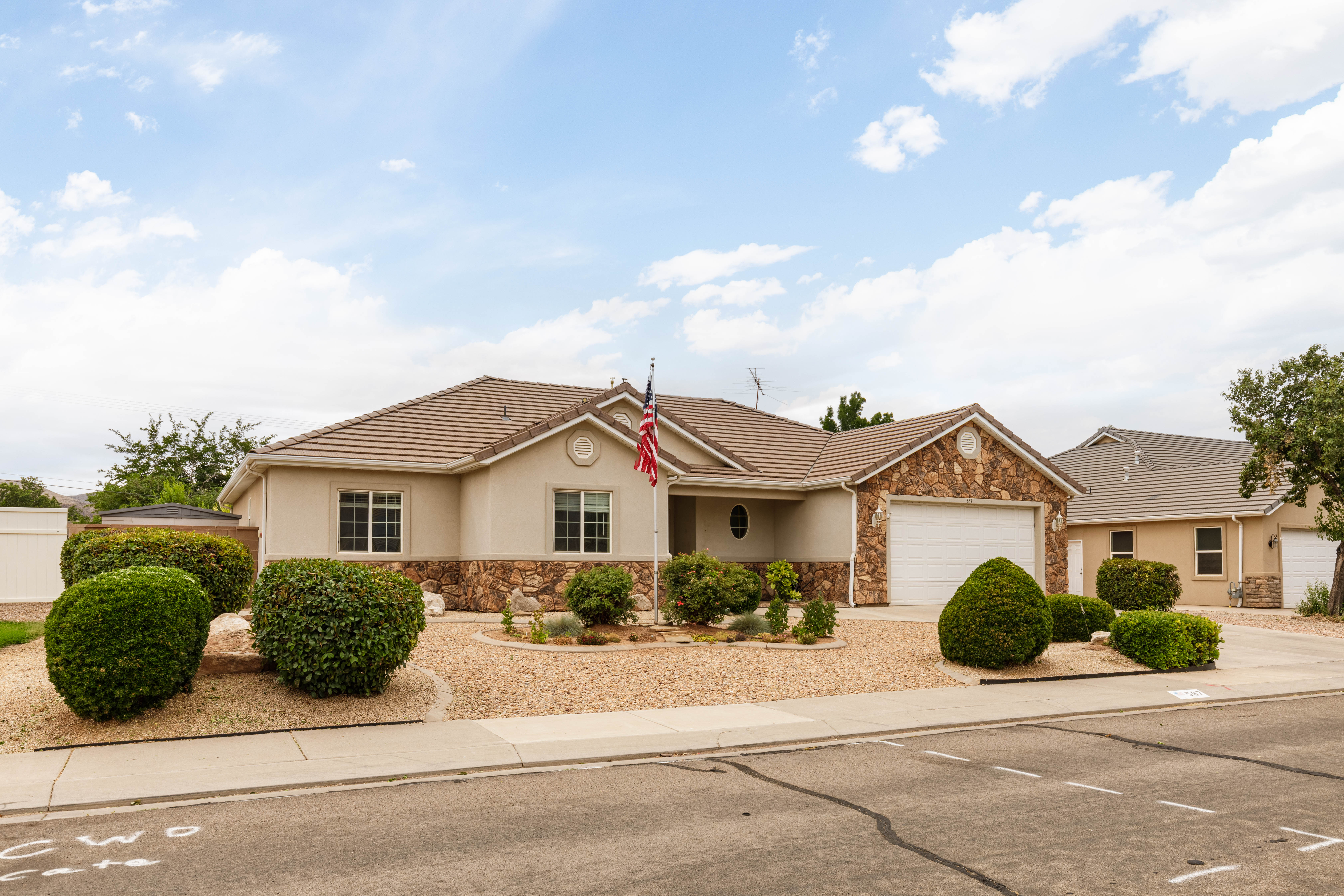 Single-story residence featuring a tile roof, stucco and stone facade, an attached garage, and a gravel and shrub front landscape