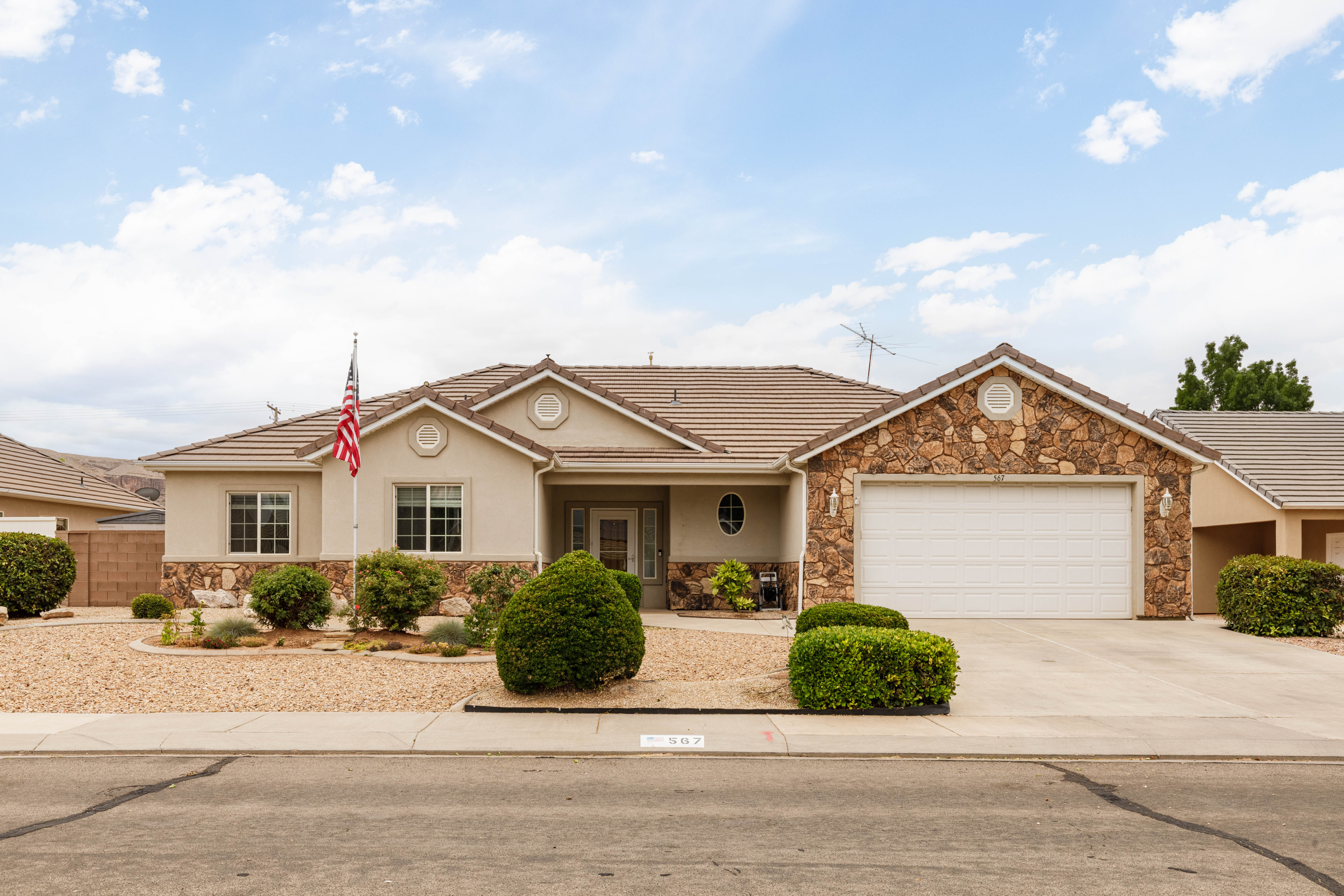 Stucco exterior with stone accents, featuring a two-car garage, concrete driveway, and mature landscaping