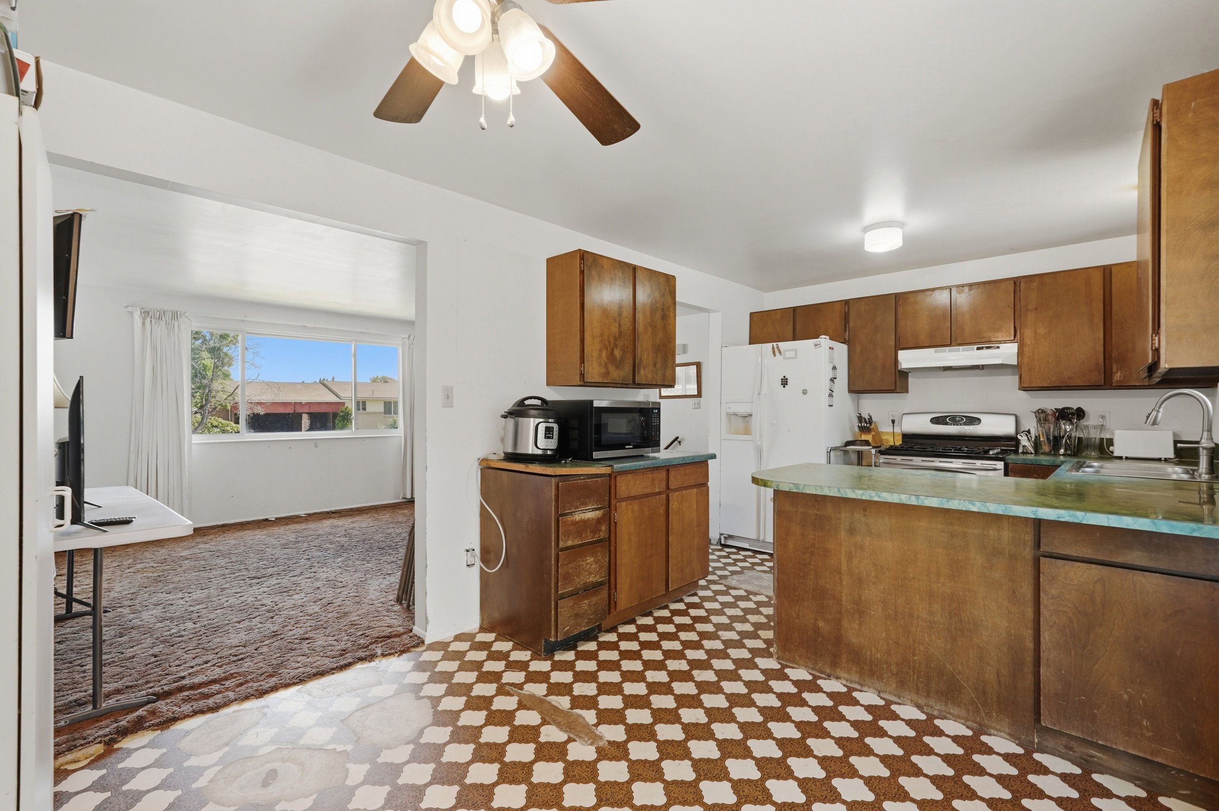Kitchen featuring wood-finish cabinetry, checked flooring, and a ceiling fan with integrated lighting