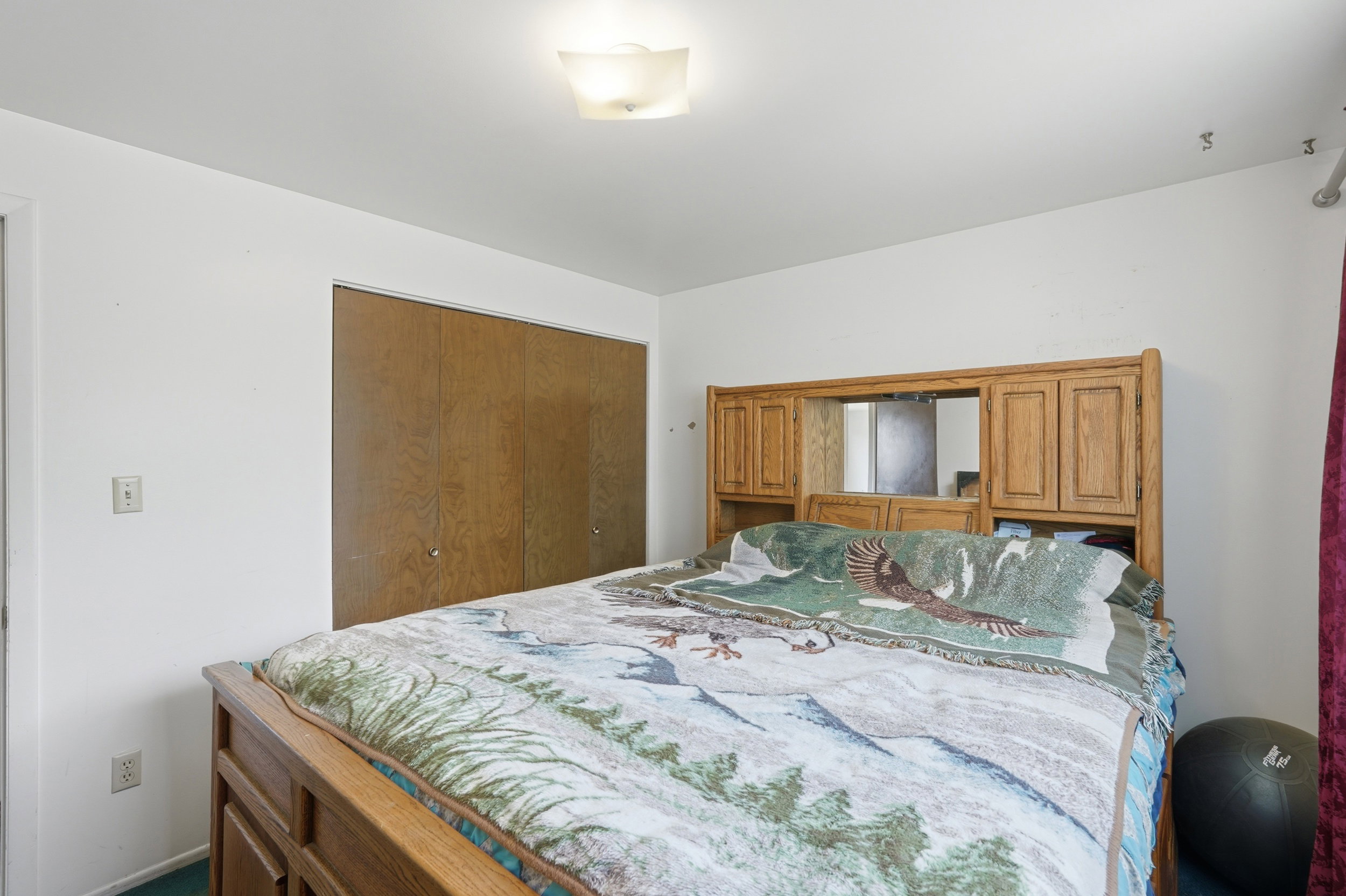 Bedroom featuring white walls, wood-finish bi-fold closet doors, a ceiling-mounted light fixture, and wall-mounted electrical outlets