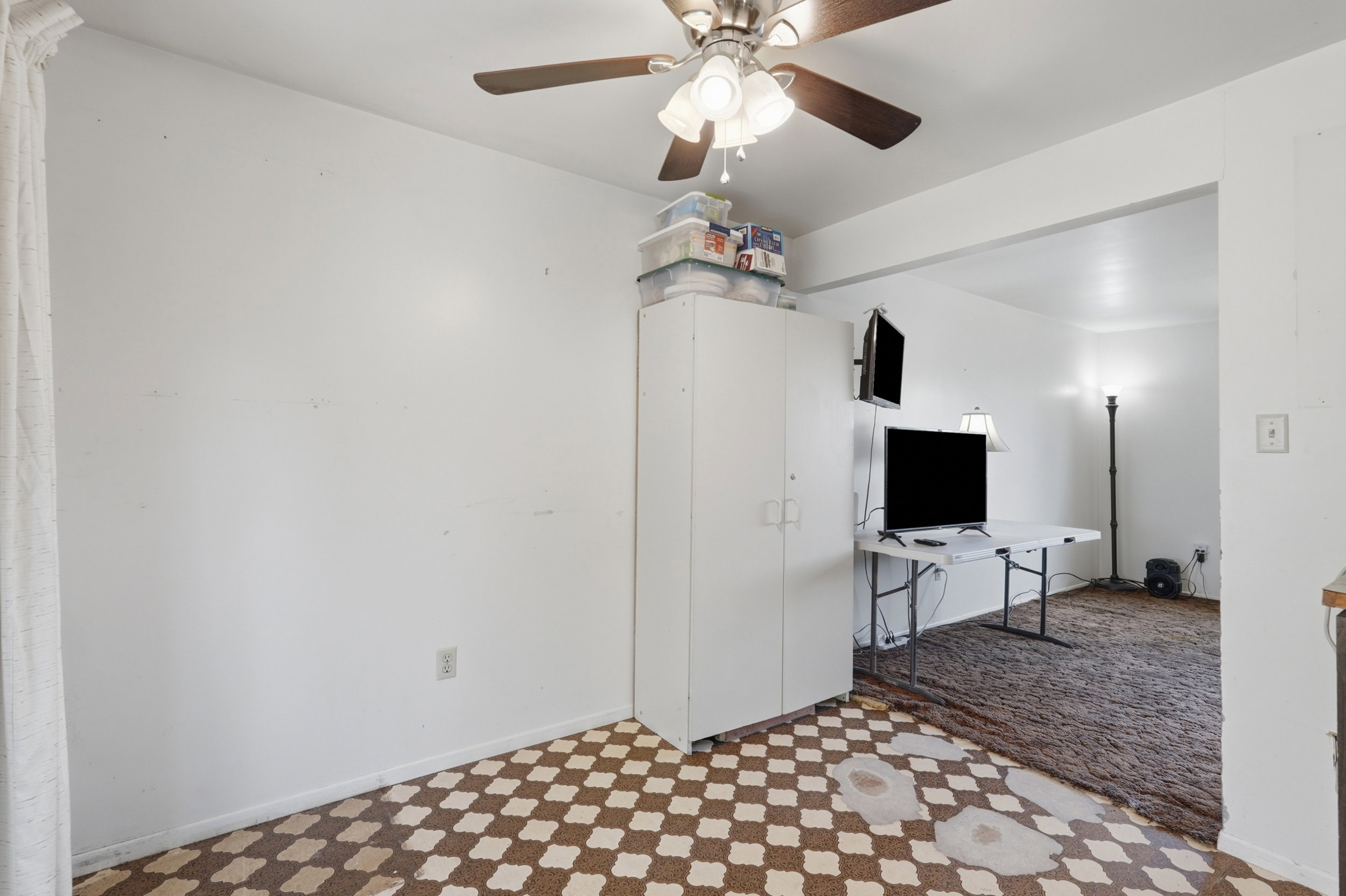 Room with patterned flooring, an overhead ceiling fan, and a built-in storage cabinet