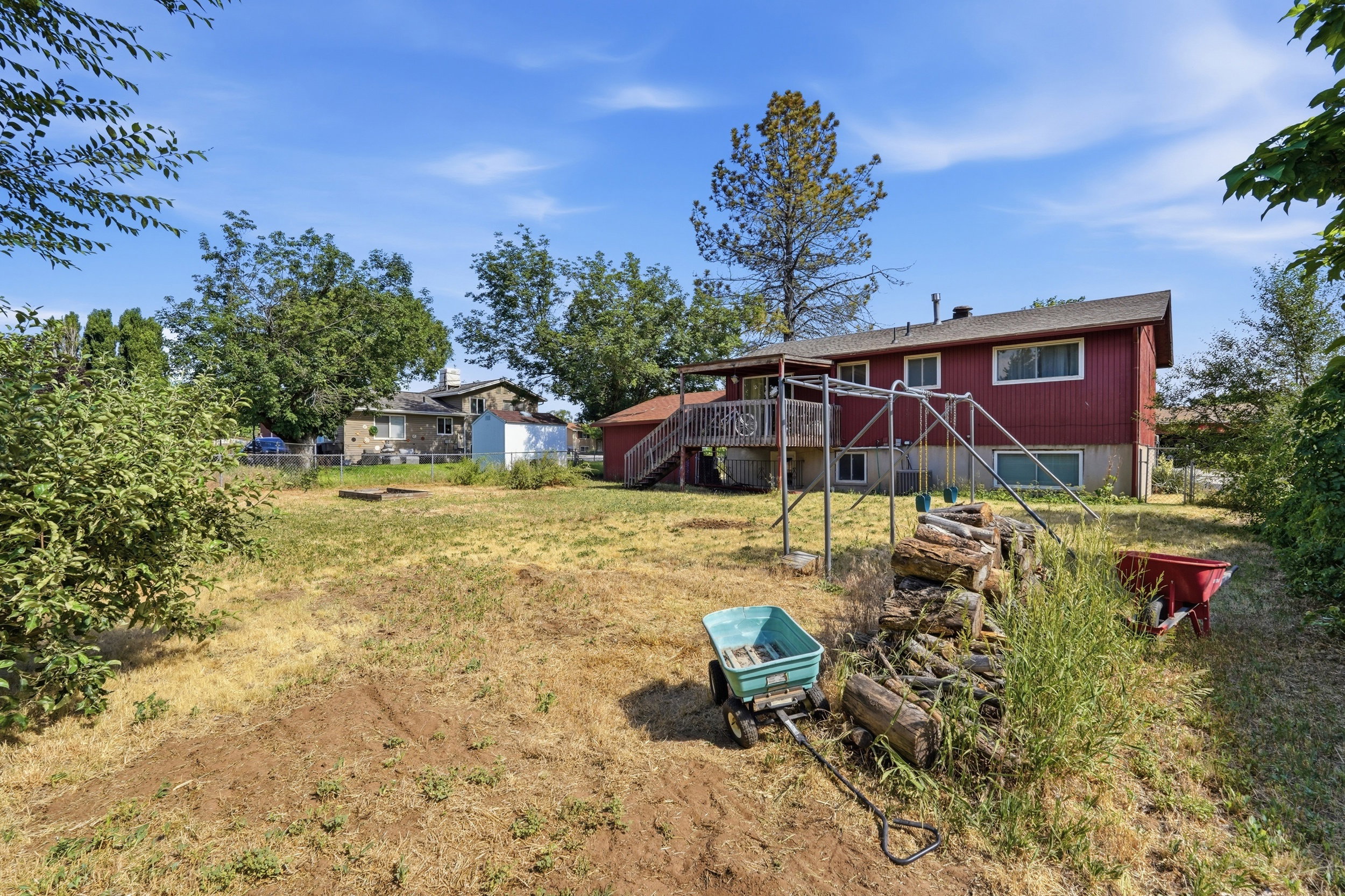 Expansive rear yard featuring a red-sided structure with a gabled roof, multiple windows, and a raised wooden deck