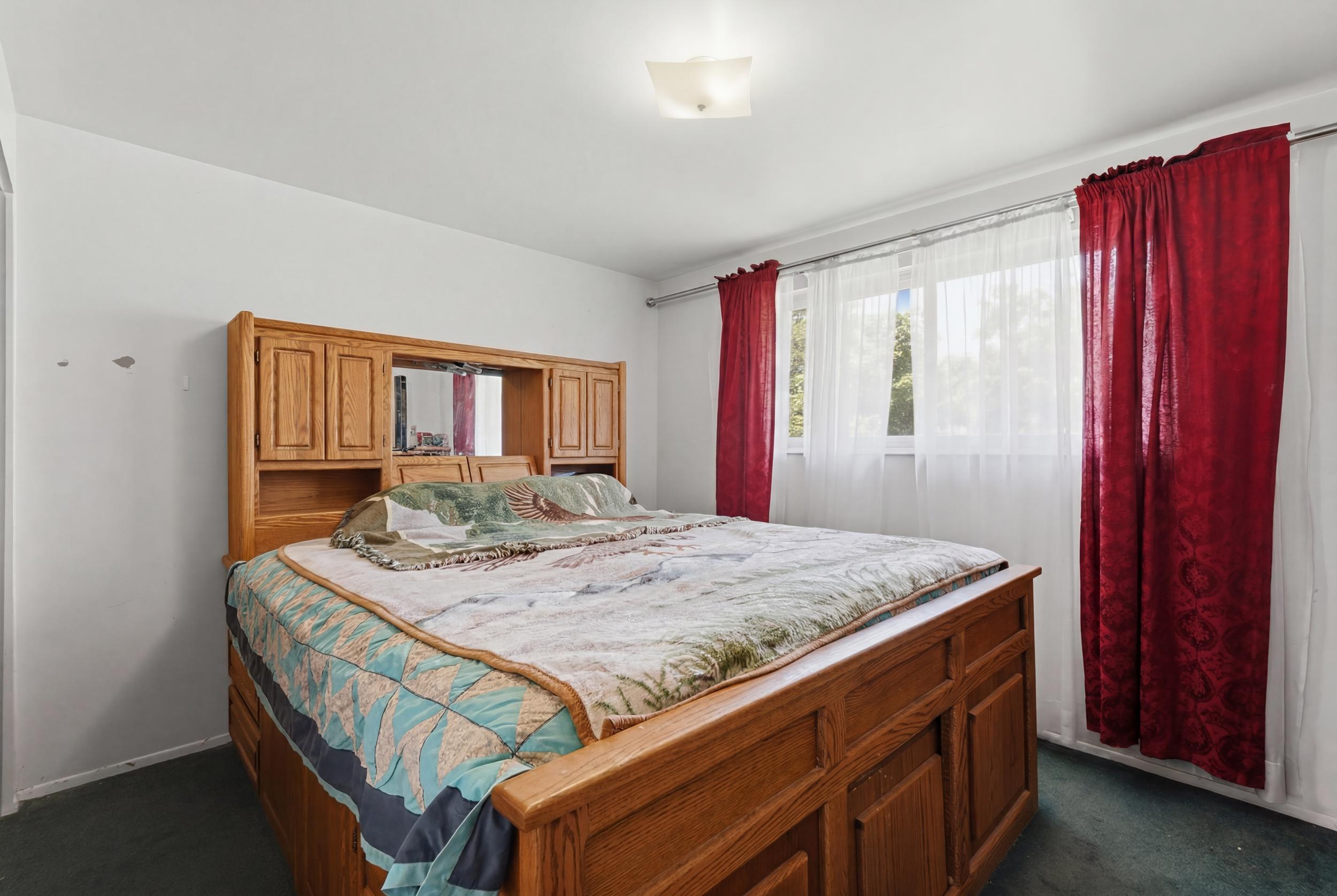 Bedroom 1 Light-filled bedroom featuring white walls, a large window with sheer and red drapes, and a ceiling-mounted light fixture