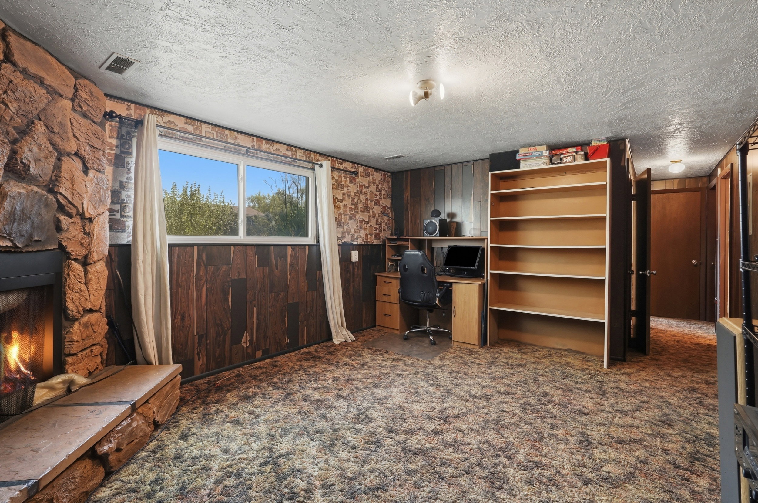 Cozy living space featuring a stone fireplace with a raised hearth, wood-finish paneling, and a built-in shelving unit