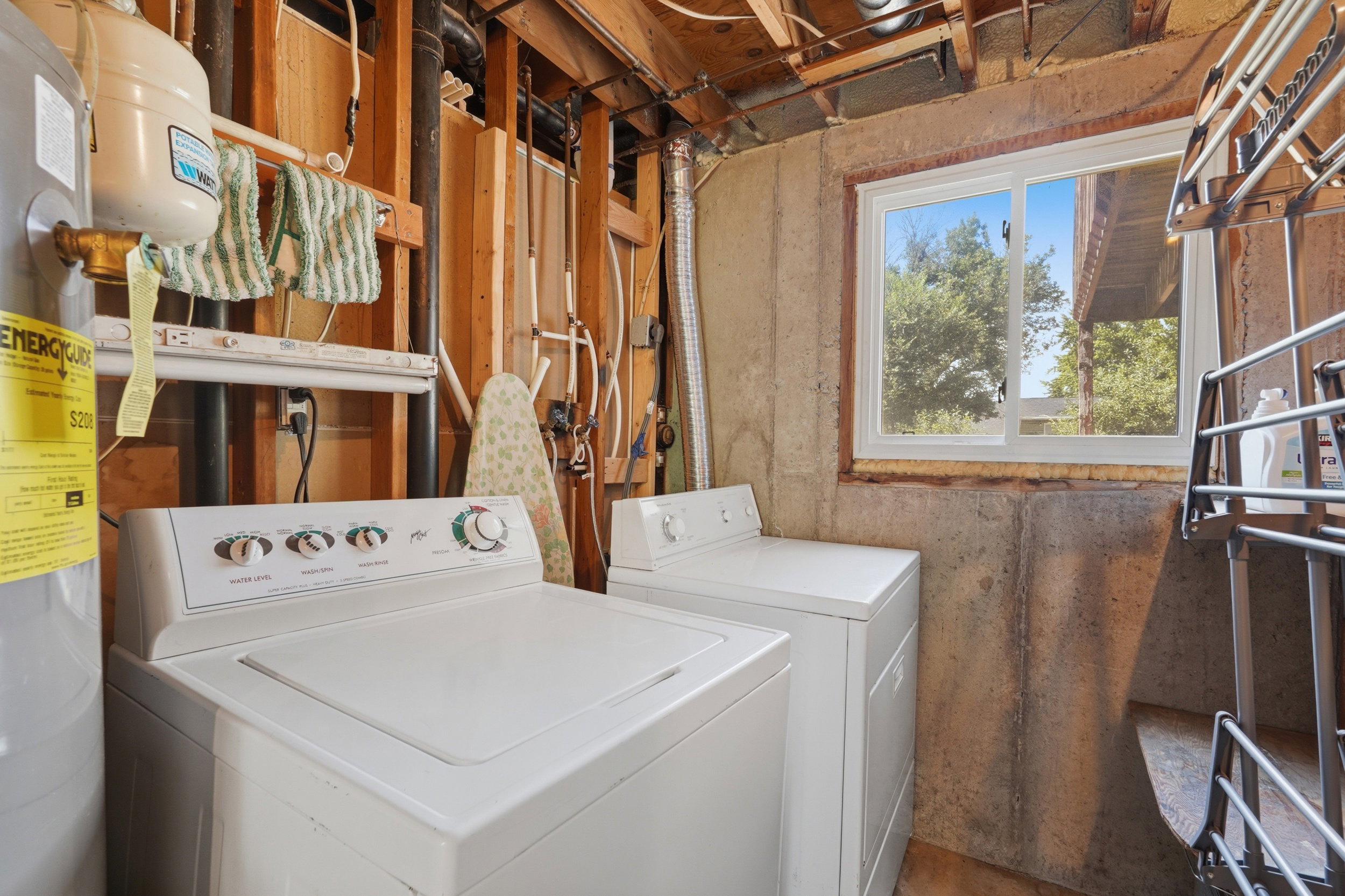 Laundry area featuring a top-load washer and dryer, a water heater, an exposed wood beam ceiling, and a sliding window