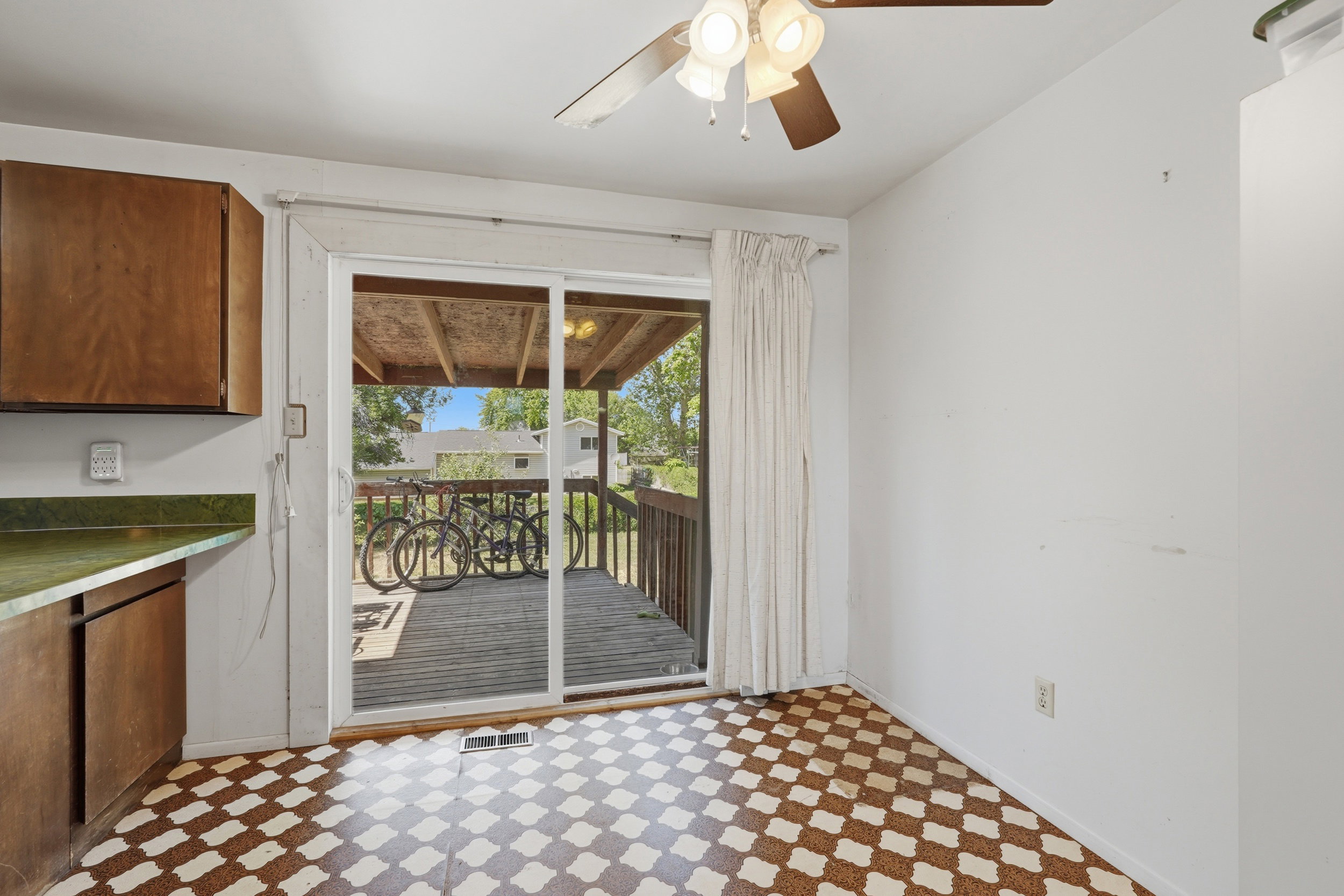 Sliding glass door opening to an exterior wood deck, featuring a ceiling fan, patterned flooring, wood-finish cabinetry, and green countertops
