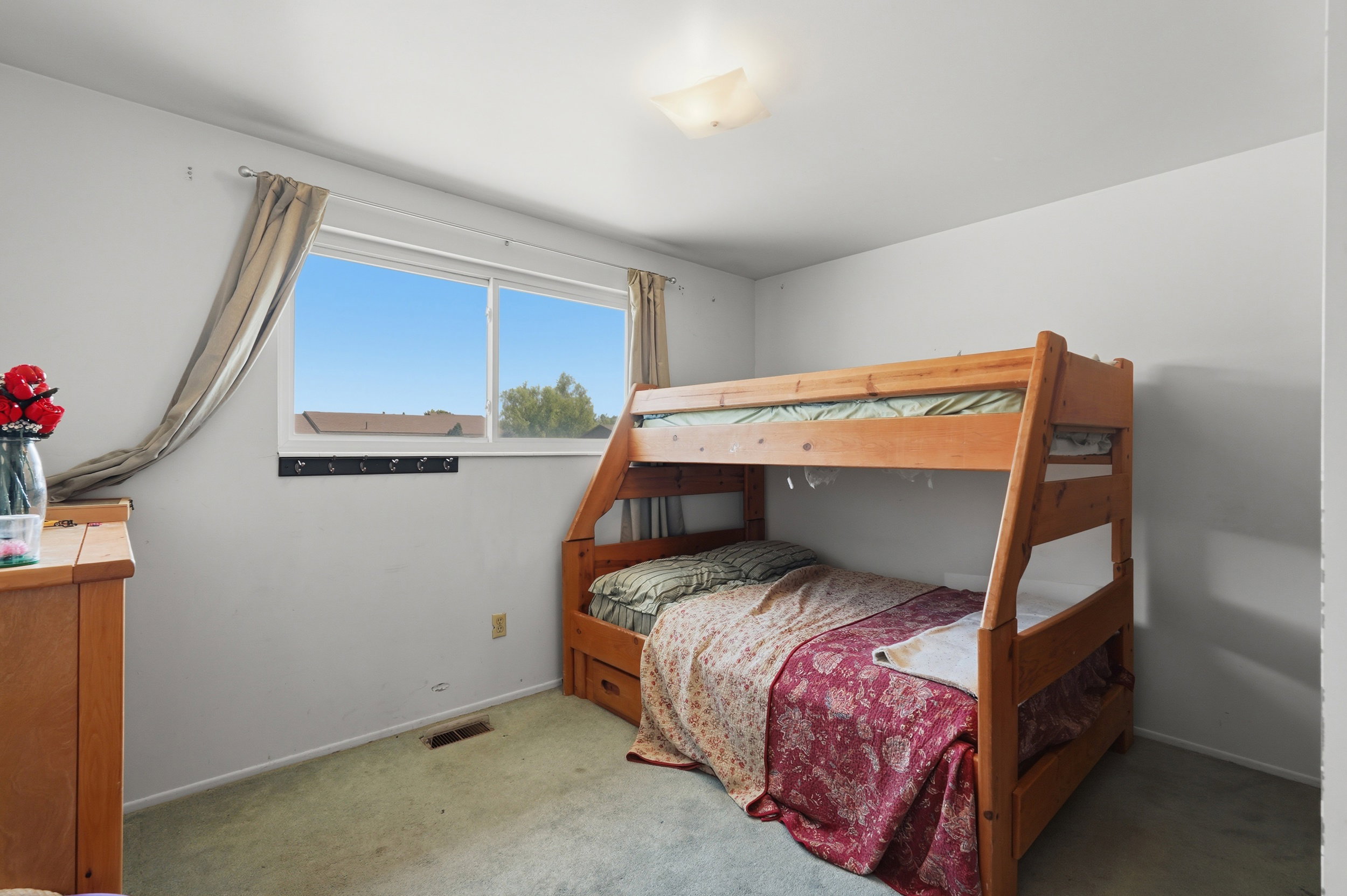 Bedroom featuring a window with a light-colored frame, a ceiling-mounted light fixture, light green carpeting, and a wall-mounted coat rack
