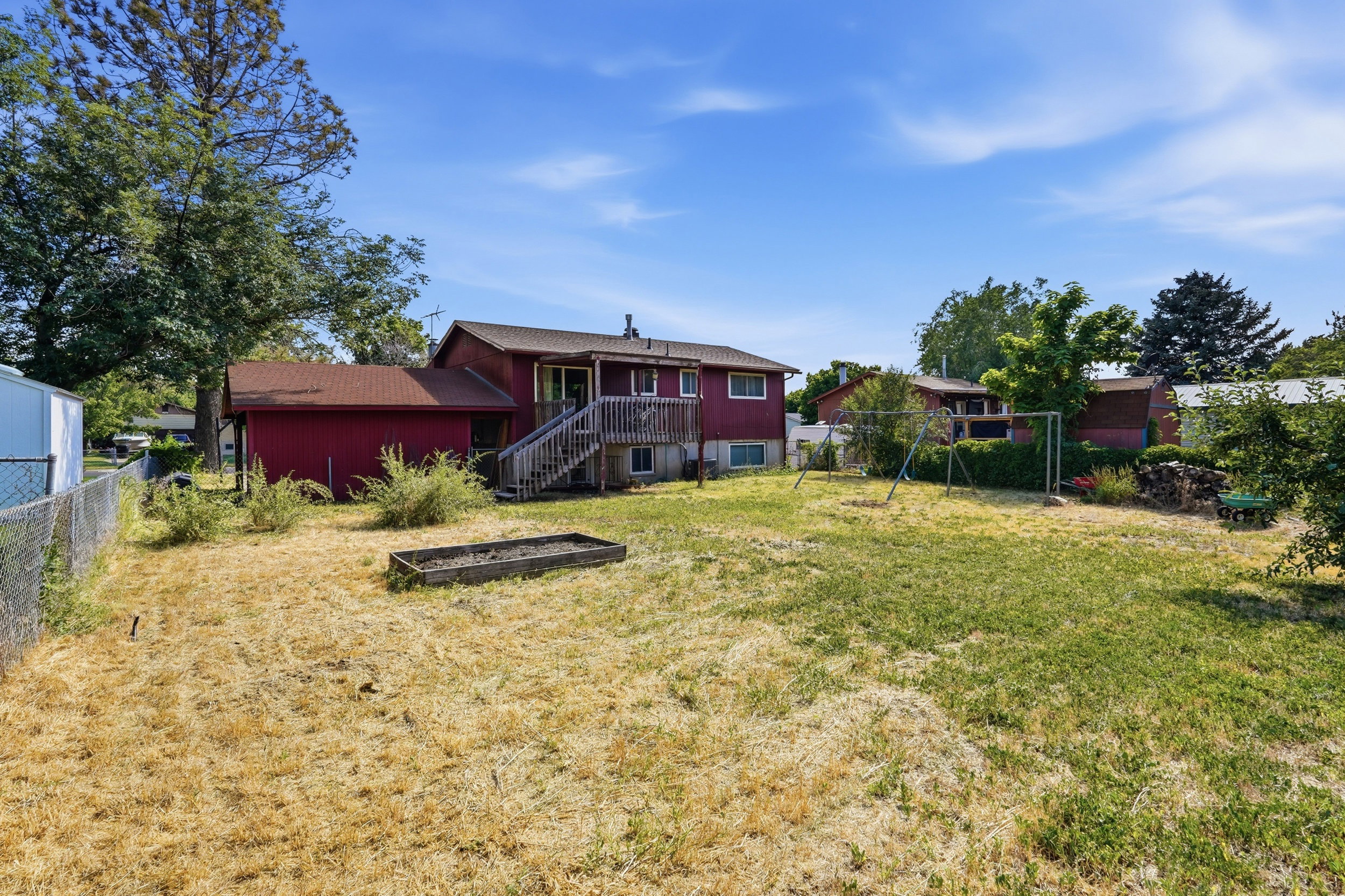Expansive backyard featuring a partial chain-link fence, mature trees, and a raised garden bed