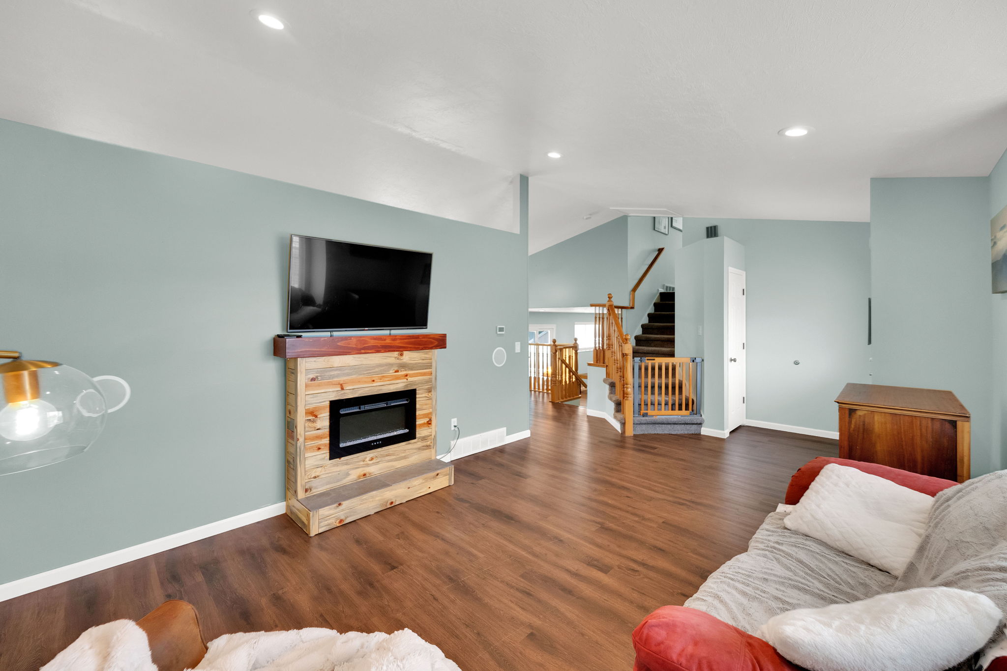 Living area featuring wood-finish flooring, a contemporary fireplace with a wood mantle, recessed lighting, and a staircase with wood railings