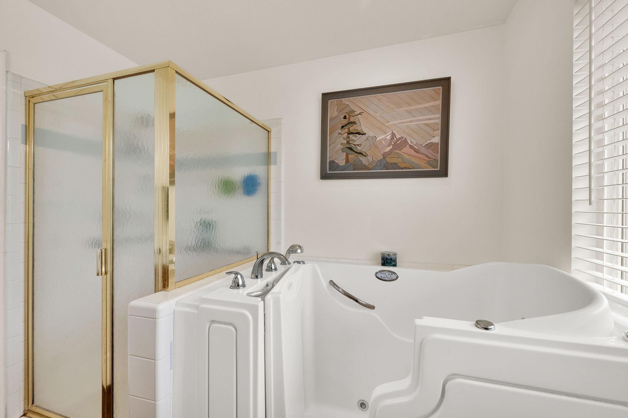 Walk-in tub with chrome fixtures, brass-framed shower enclosure, and white horizontal blinds