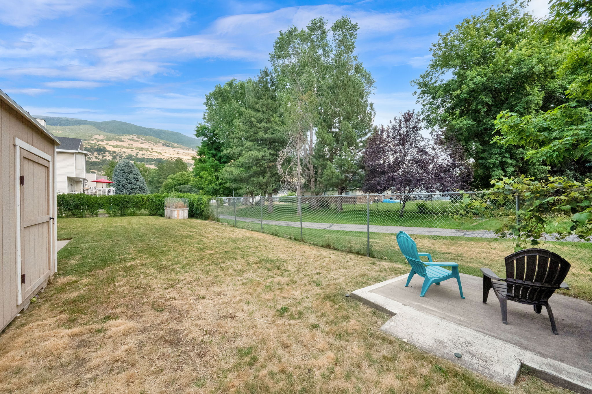 Expansive backyard with a concrete patio, wood-sided storage shed, and chain-link fencing