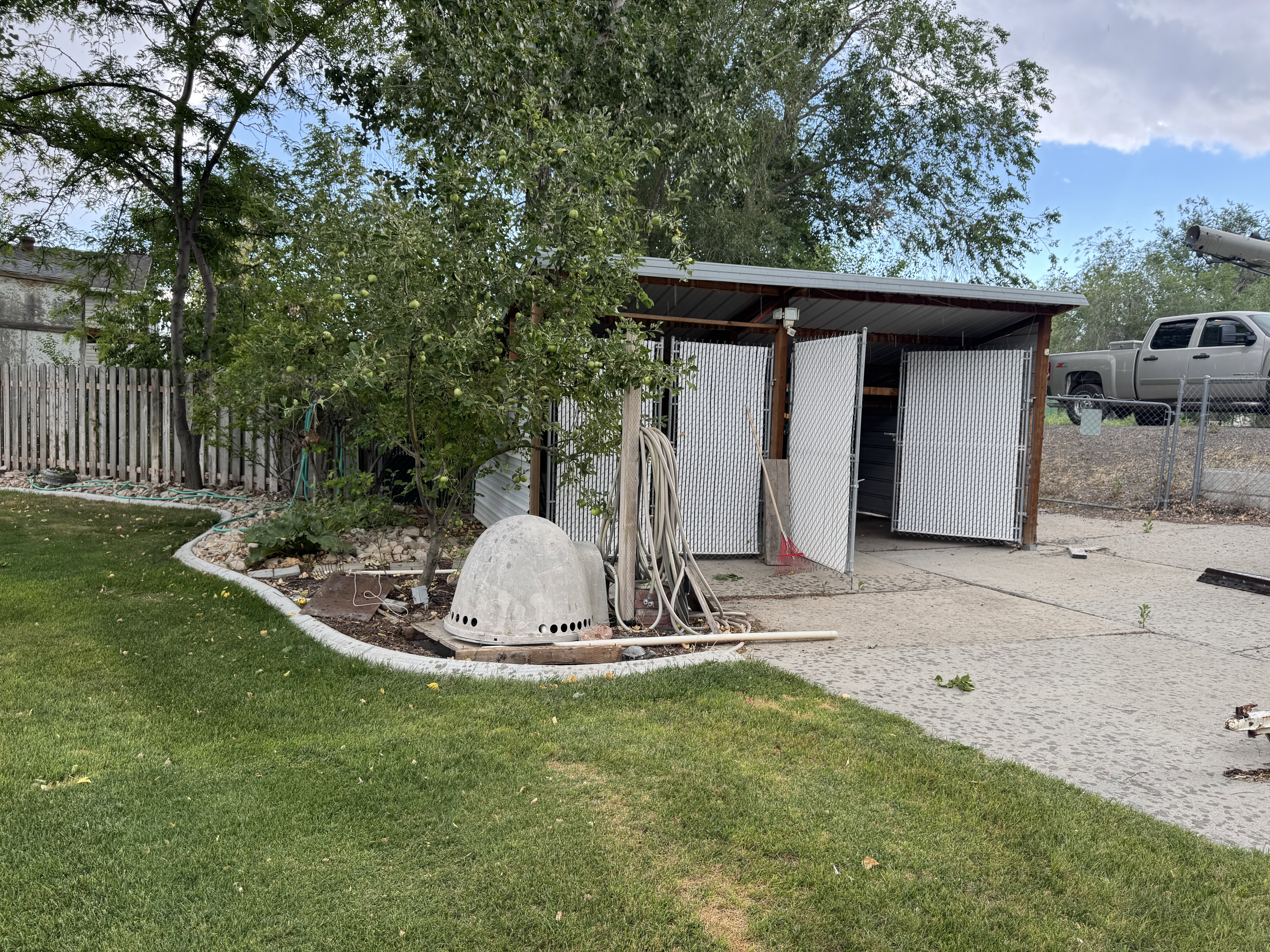 Covered structure with three bay openings, concrete ground, and partial chain link fencing