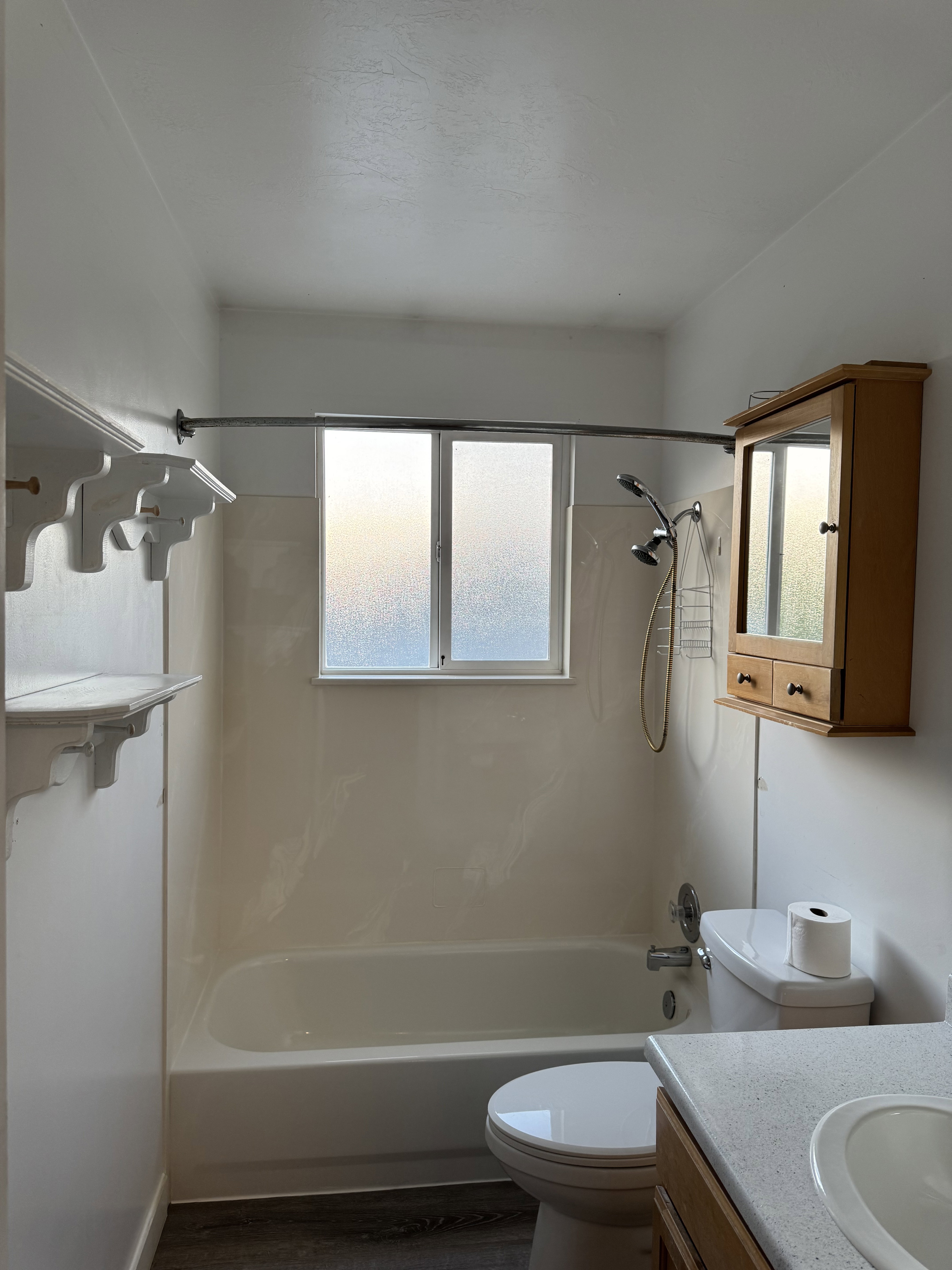 Bathroom featuring a white bathtub with a window, wood-finish flooring, a toilet, a vanity with an integrated sink, and a wall-mounted medicine cabinet