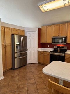 Kitchen featuring stainless steel appliances, wood-finish cabinetry, tile flooring, light-toned countertops, and a white paneled door