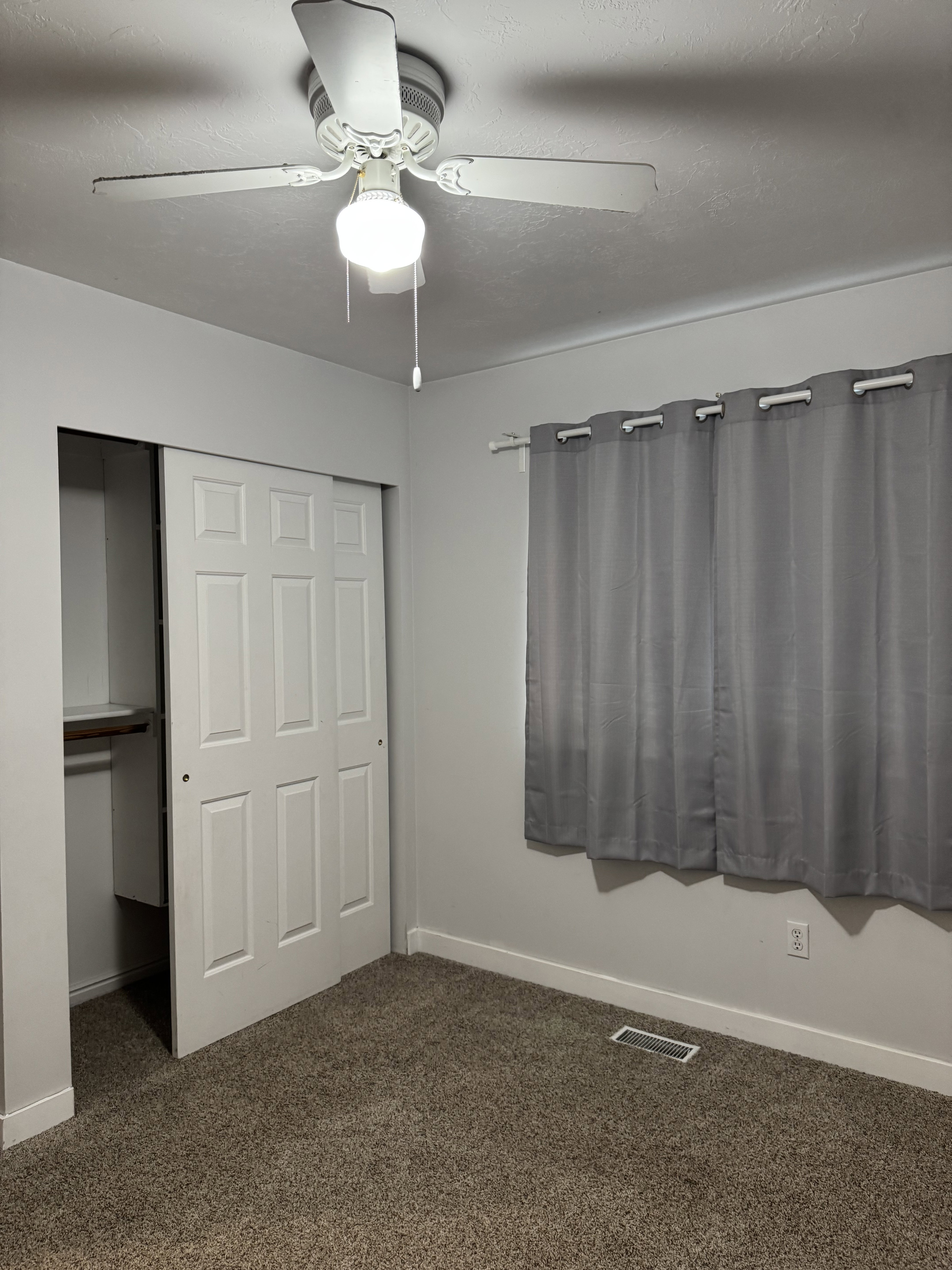 Interior room featuring neutral wall paint, textured carpeting, and a ceiling fan with integrated lighting
