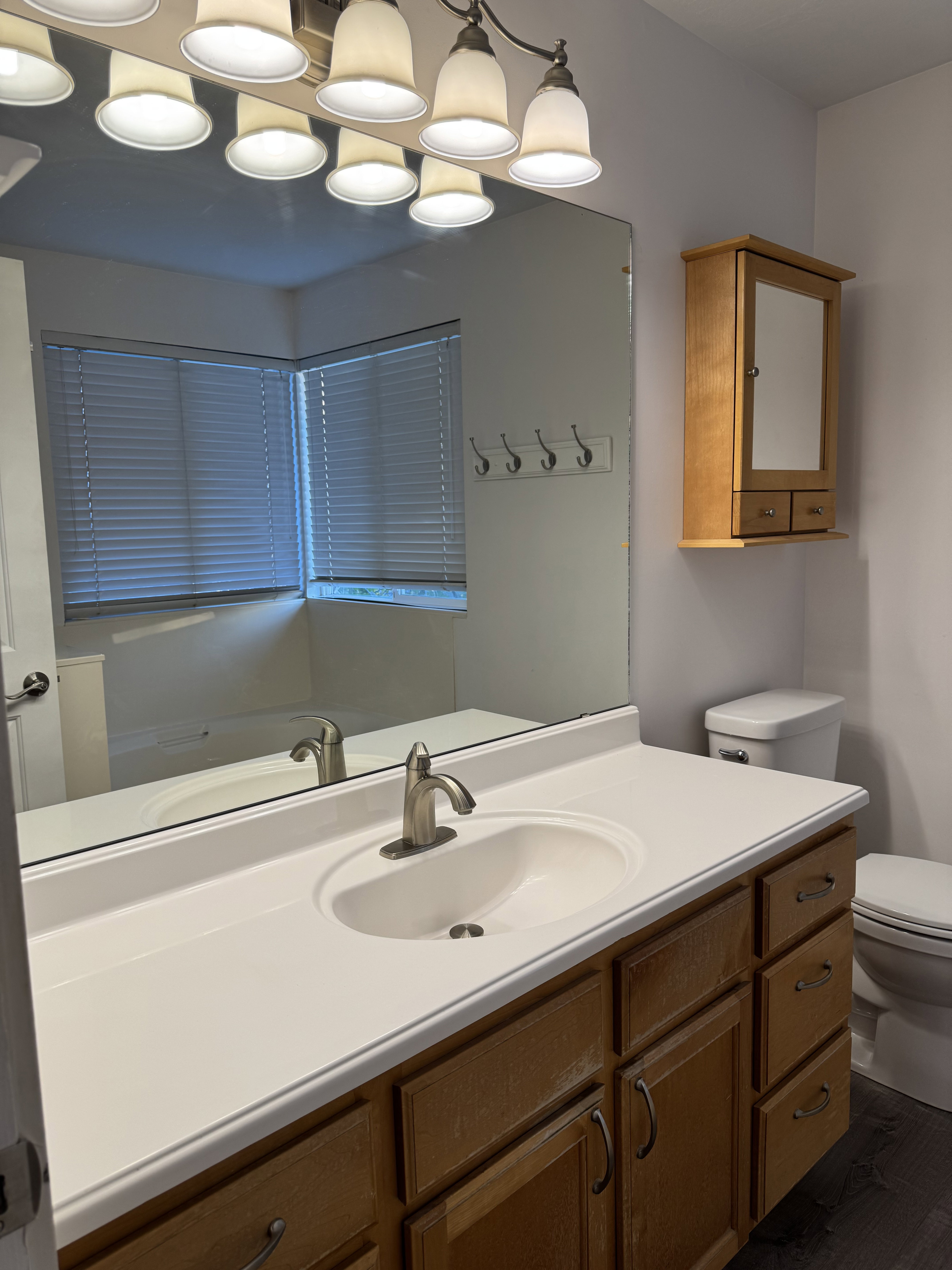 Bathroom vanity featuring a white solid surface countertop with an integrated sink, brushed nickel faucet, and wood-finish cabinetry