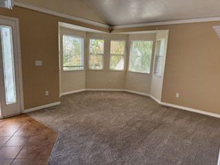 Spacious interior featuring a large bay window, vaulted ceiling, neutral wall tones, and plush carpeting