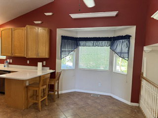 Kitchen area with a bay window, wood cabinetry, L-shaped counter, and tile flooring