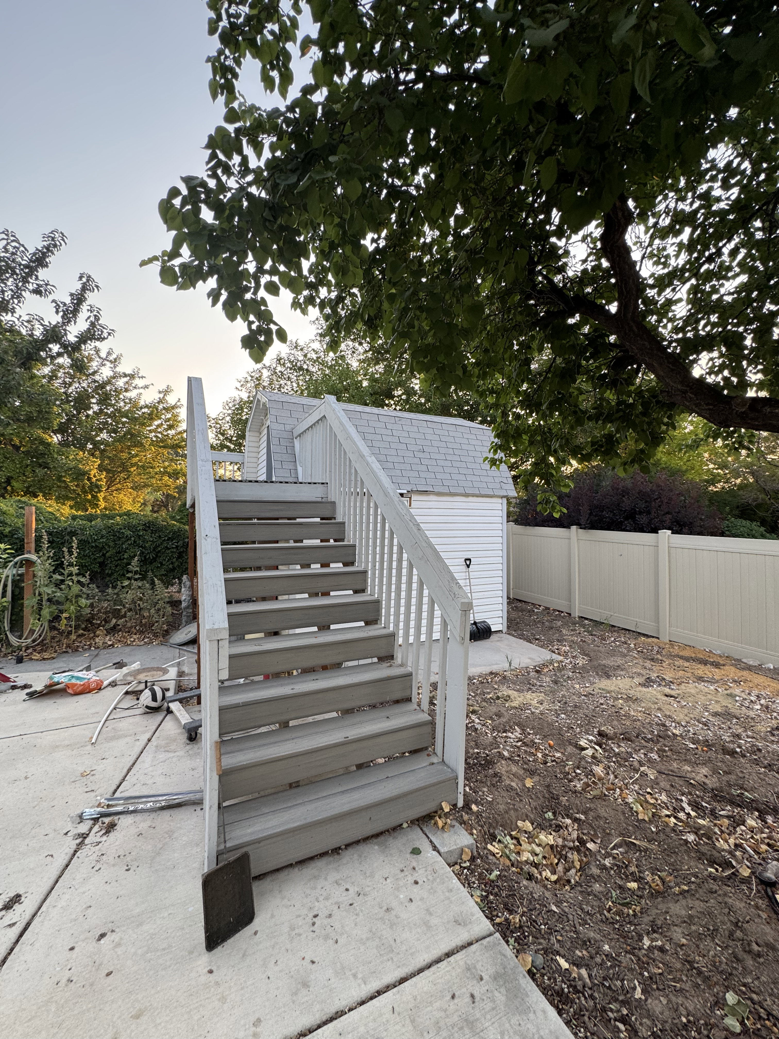 Outdoor stairs with white railings and gray treads, leading to a storage shed with white siding and a gray shingled roof