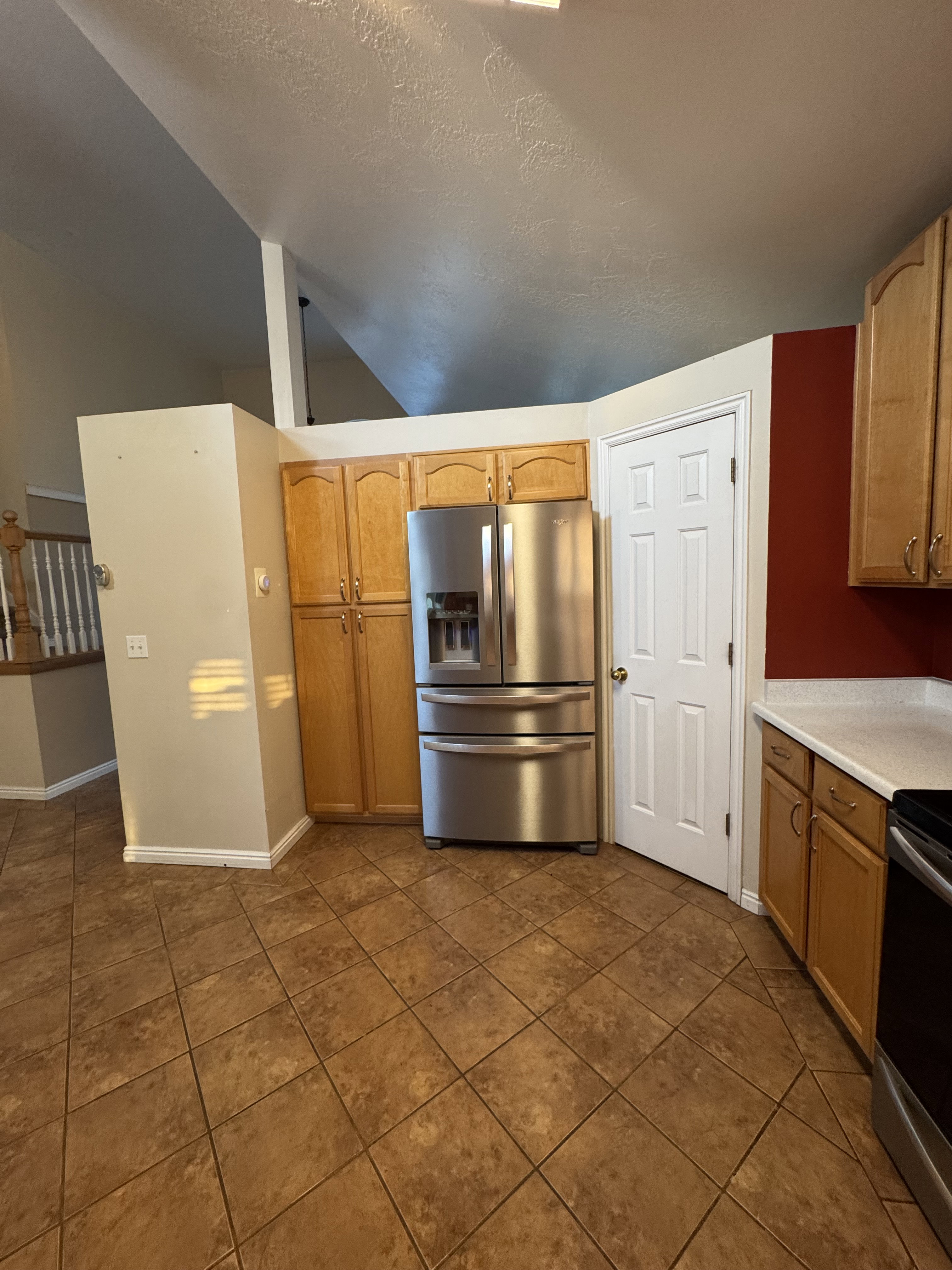 Kitchen area featuring stainless steel refrigerator, wood-finish cabinetry, light-toned countertops, and large format tile flooring