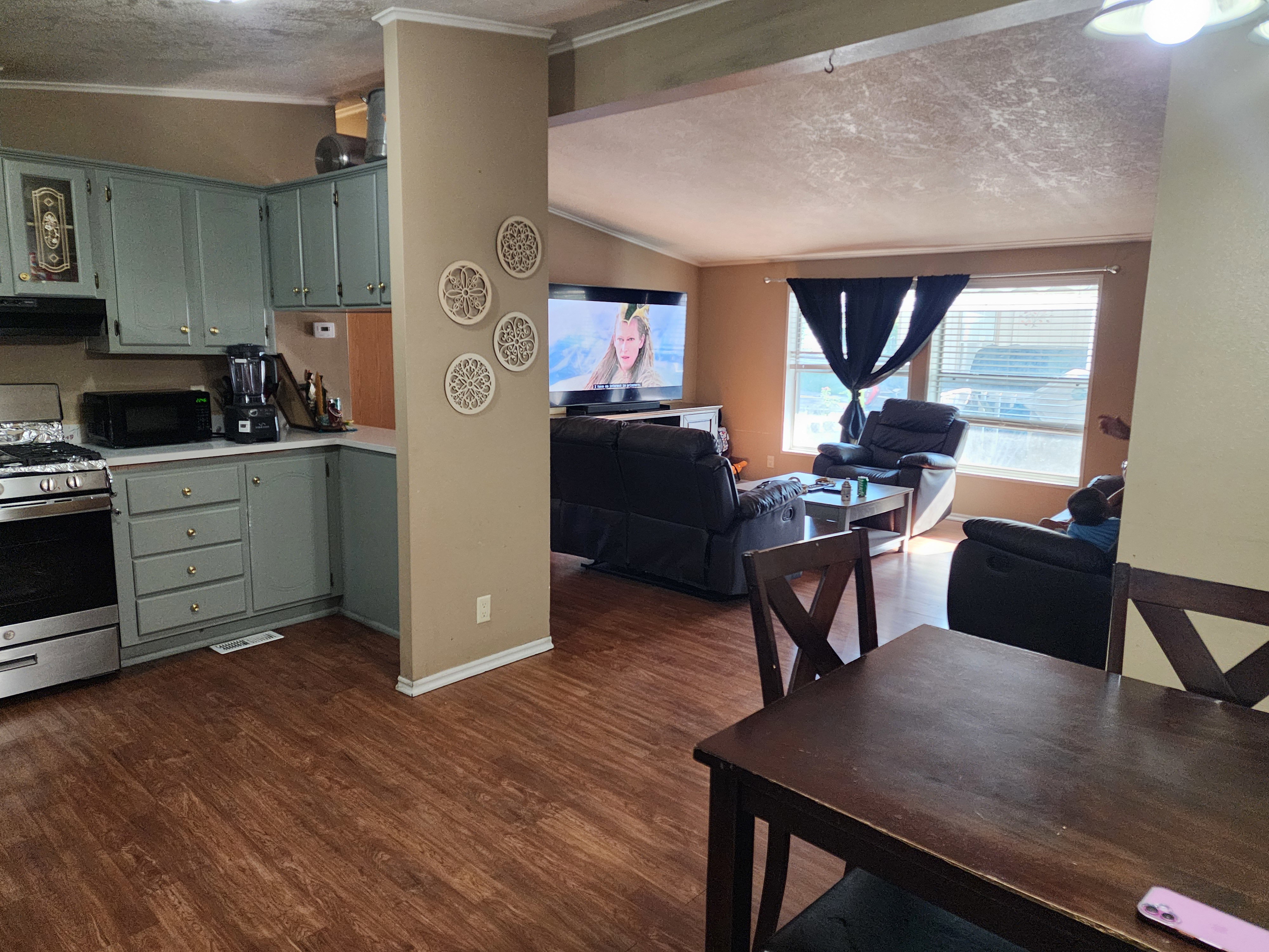 Open-concept living area featuring wood-finish flooring, a kitchen with light blue cabinetry, stainless steel range, and a breakfast bar