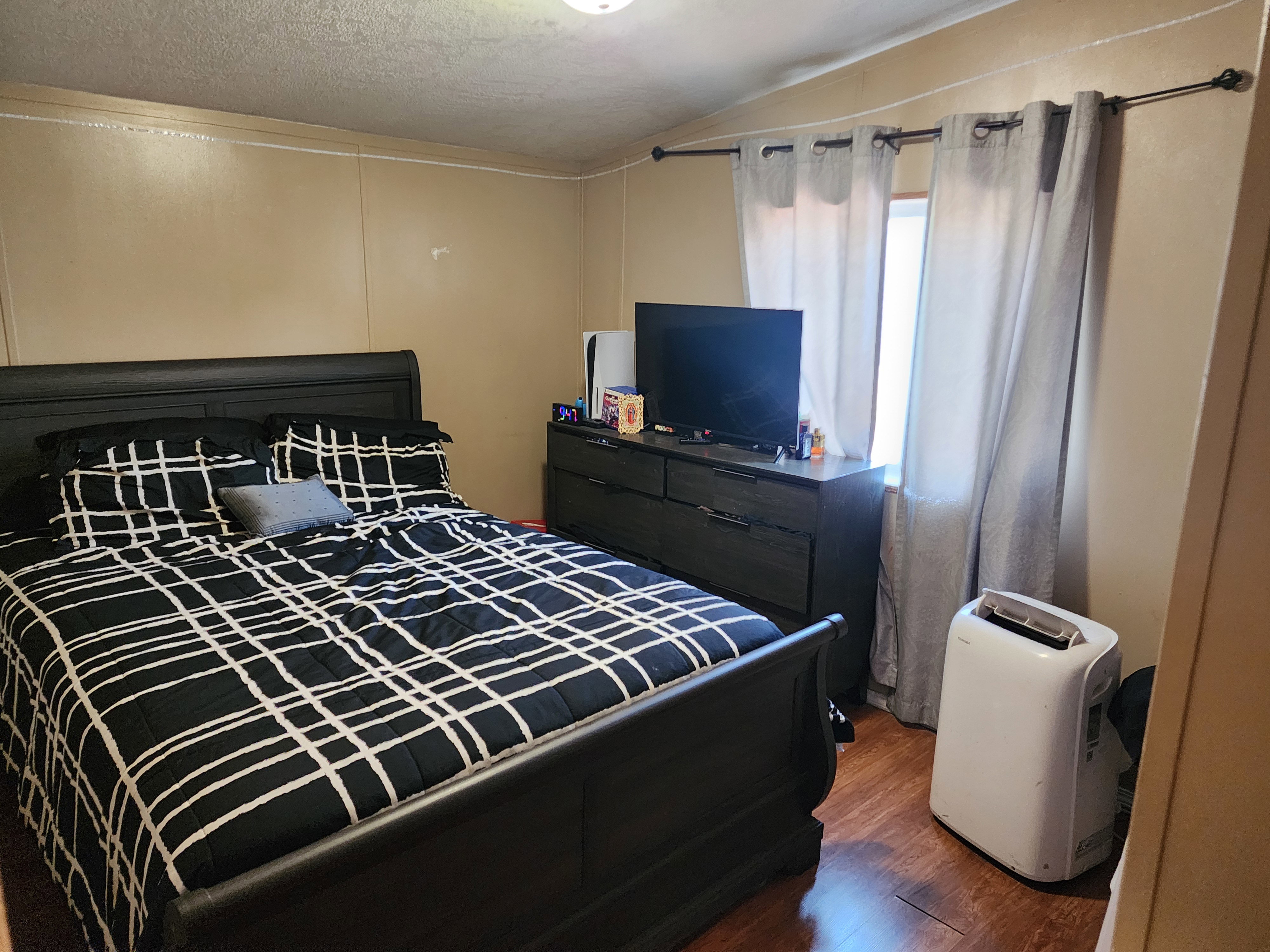 Bedroom featuring wood-finish flooring, a neutral wall color, and a window with curtain rod