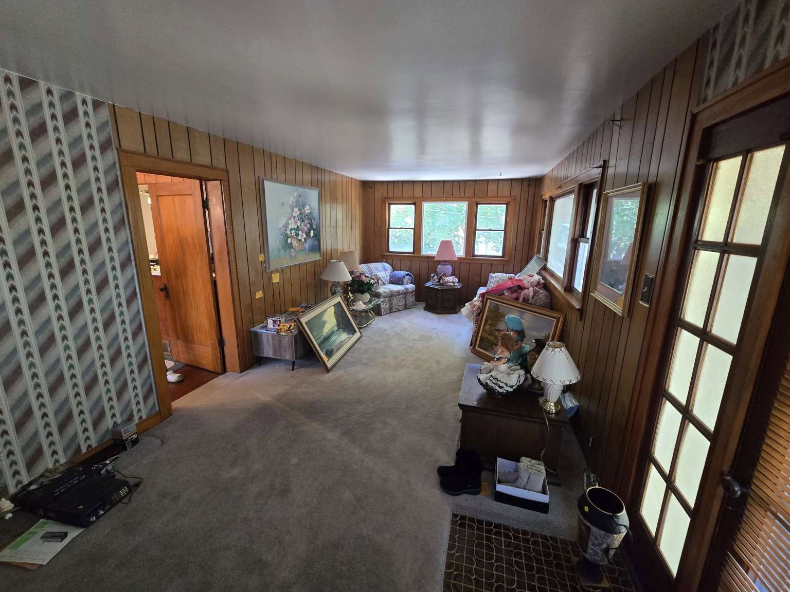 Room featuring wood-paneled walls, multiple windows, a paneled door, and carpeting