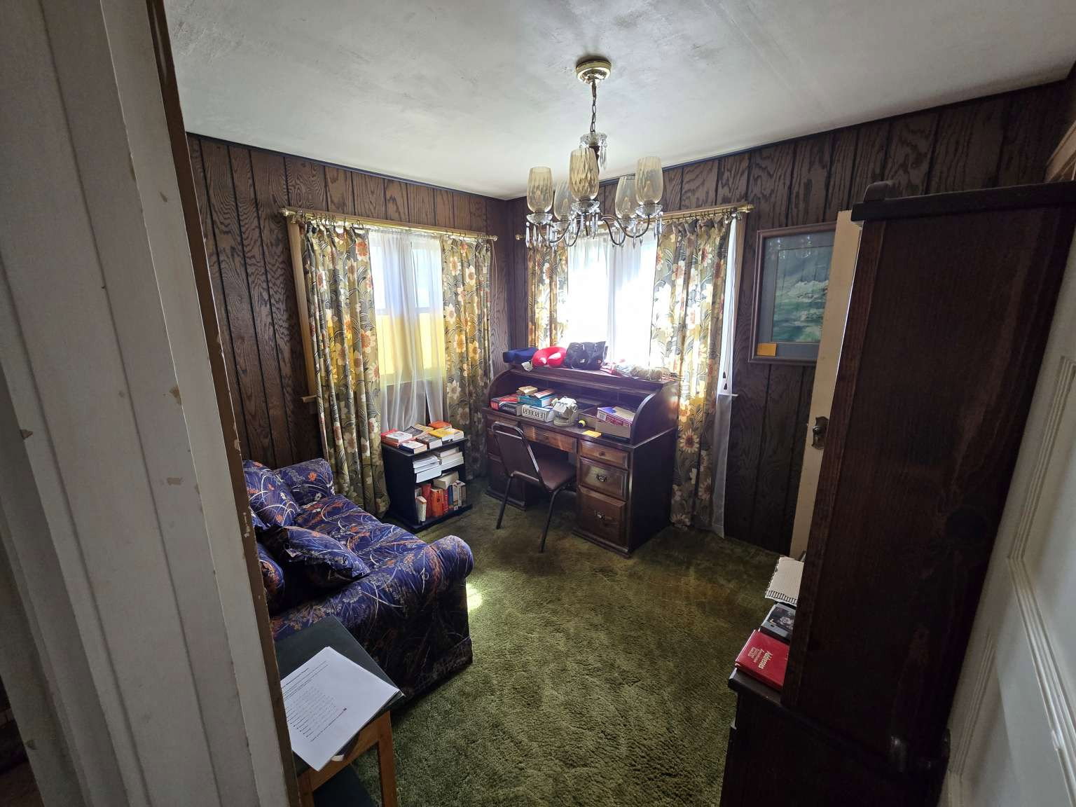 Interior room featuring wood-panel walls, wall-to-wall green carpeting, and a central chandelier