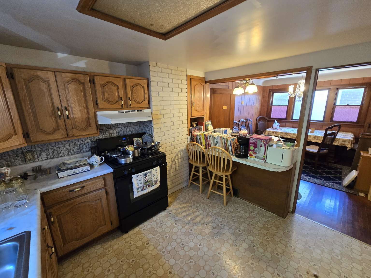 Kitchen featuring wood cabinetry, a white countertop, a black range with an overhead vent, and patterned flooring