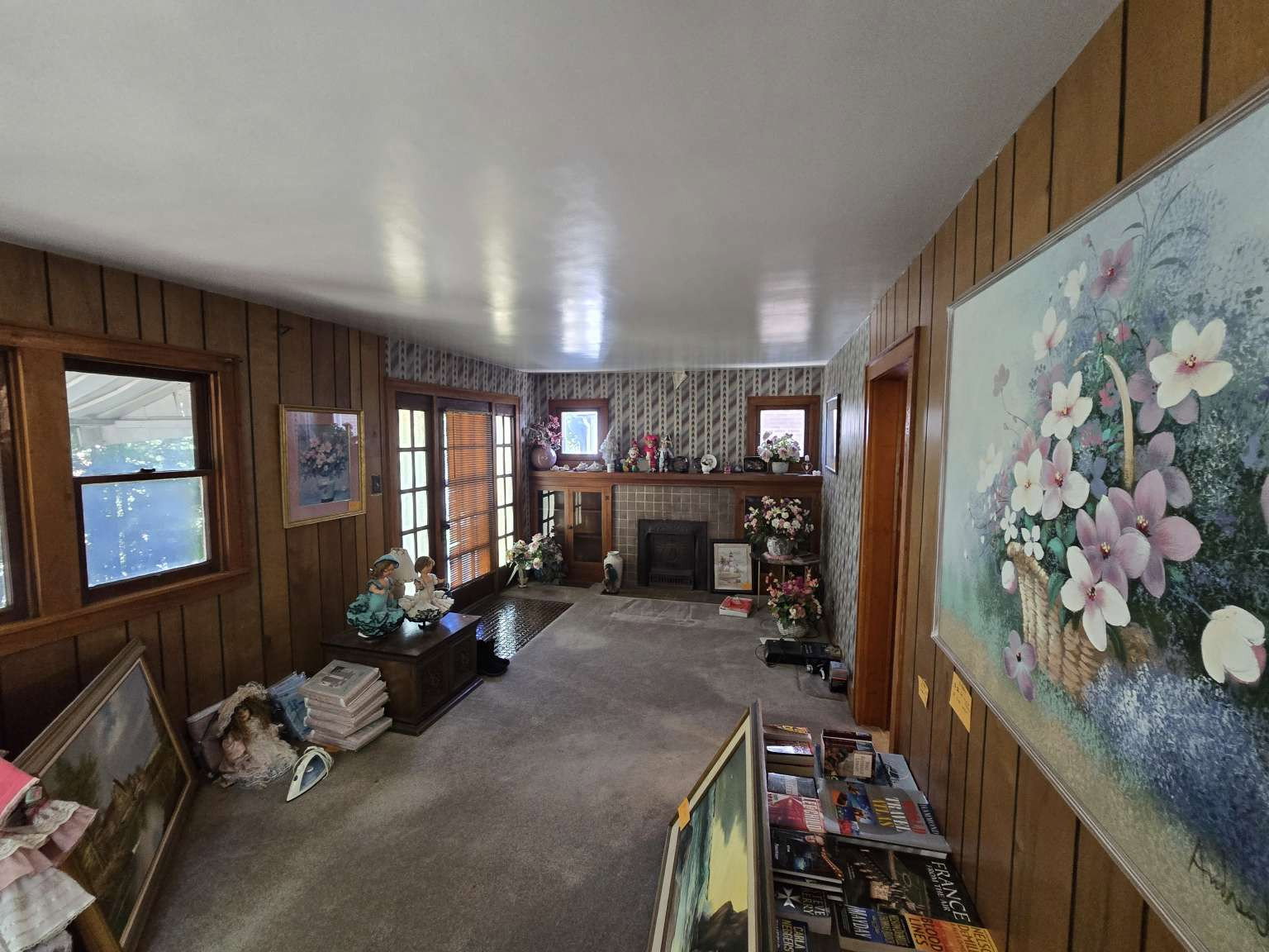 Living area featuring wood paneling, multiple windows with wood trim, a central fireplace with a brick hearth, and a glass-paneled double door
