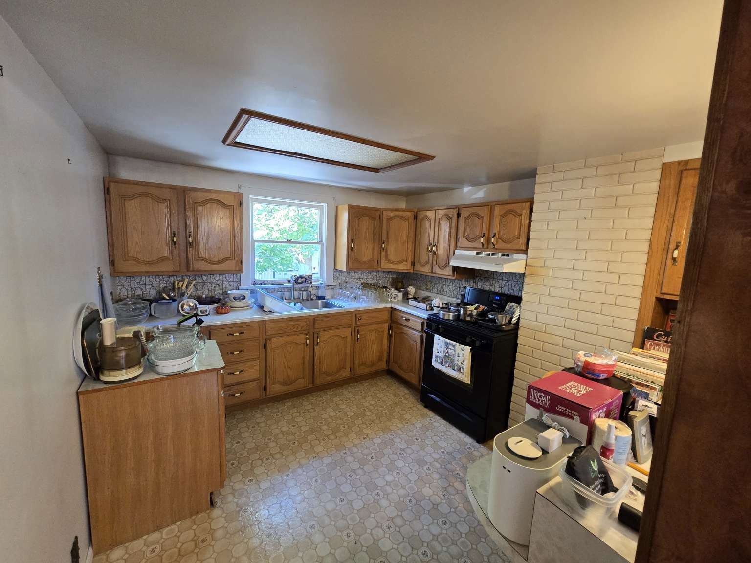 Kitchen featuring wood cabinetry, a window over the sink, a white countertop, and a black range with an overhead vent
