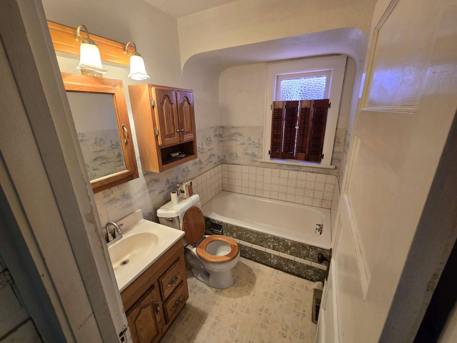 Full bathroom featuring a white porcelain bathtub, white tile surround, and a wood-finish vanity with an integrated sink