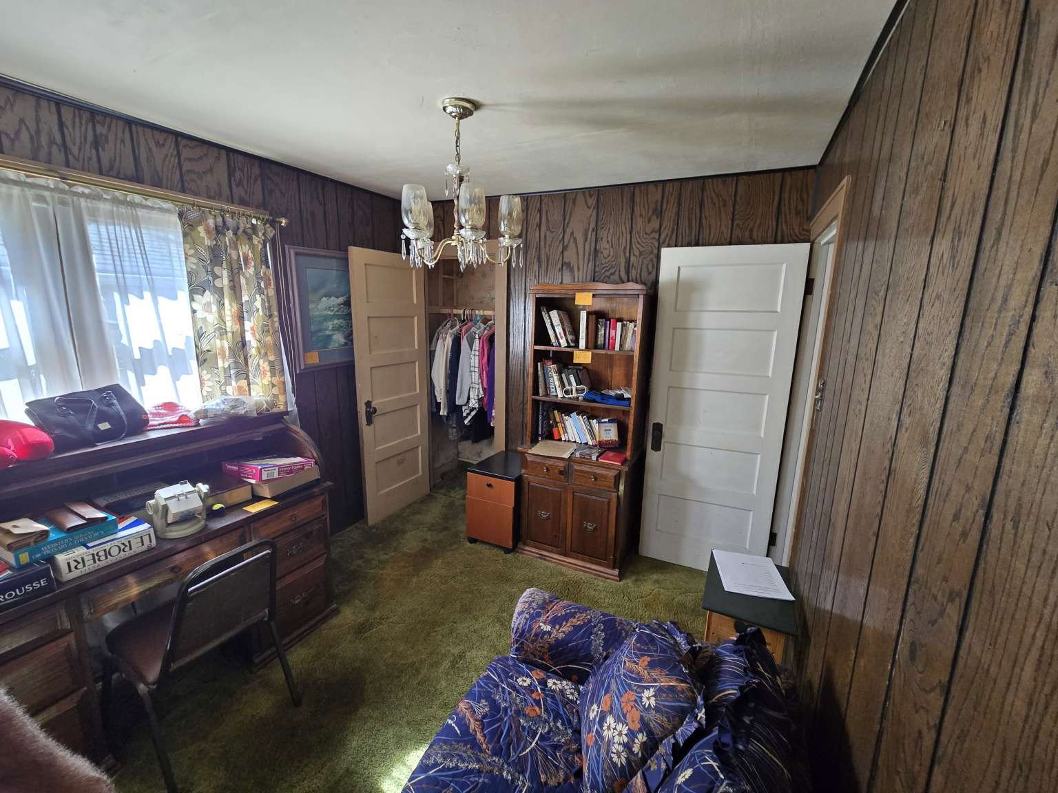 Room featuring wood-paneled walls, green carpet flooring, and a multi-light chandelier