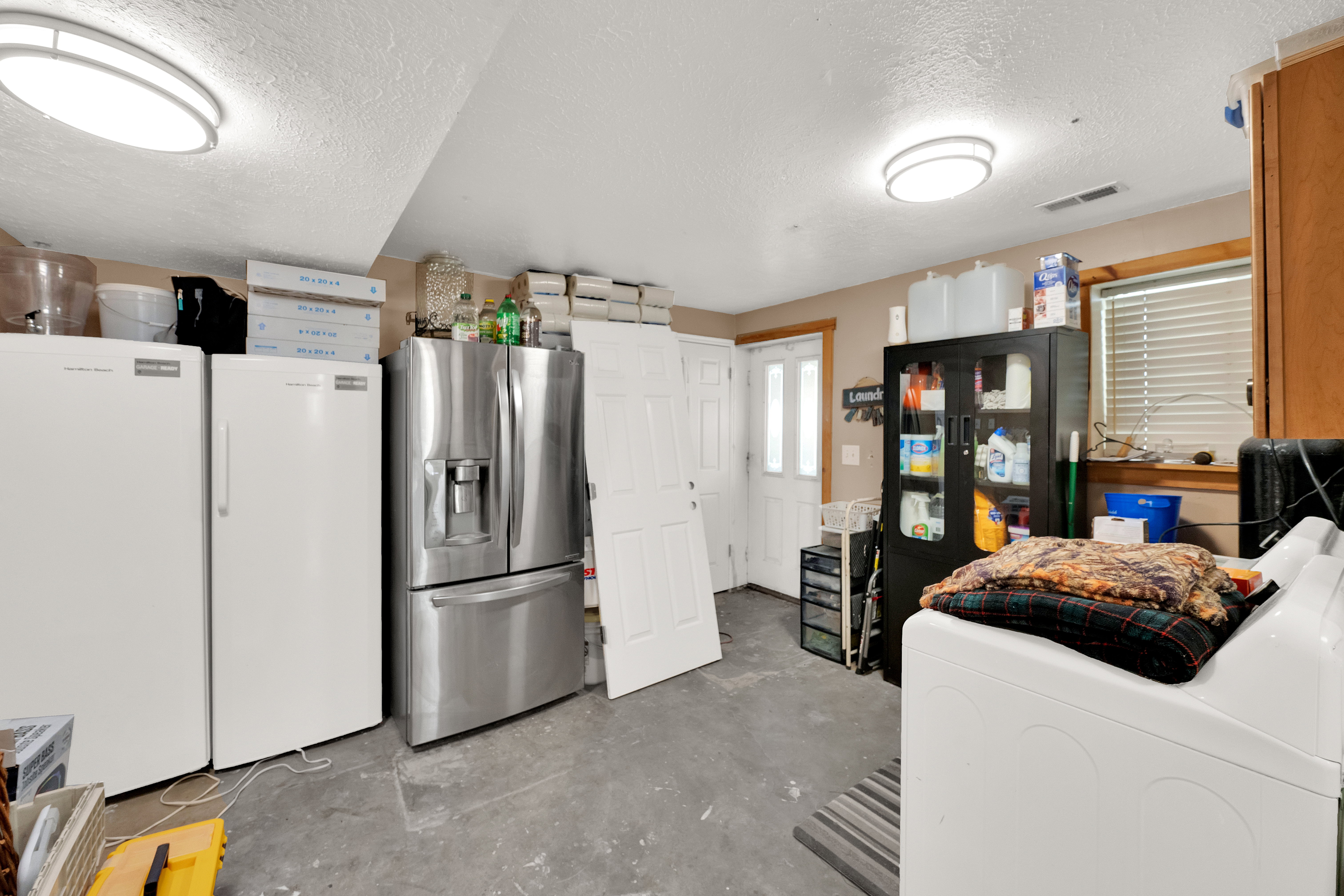 Utility room with concrete flooring, dual ceiling light fixtures, and a white paneled door