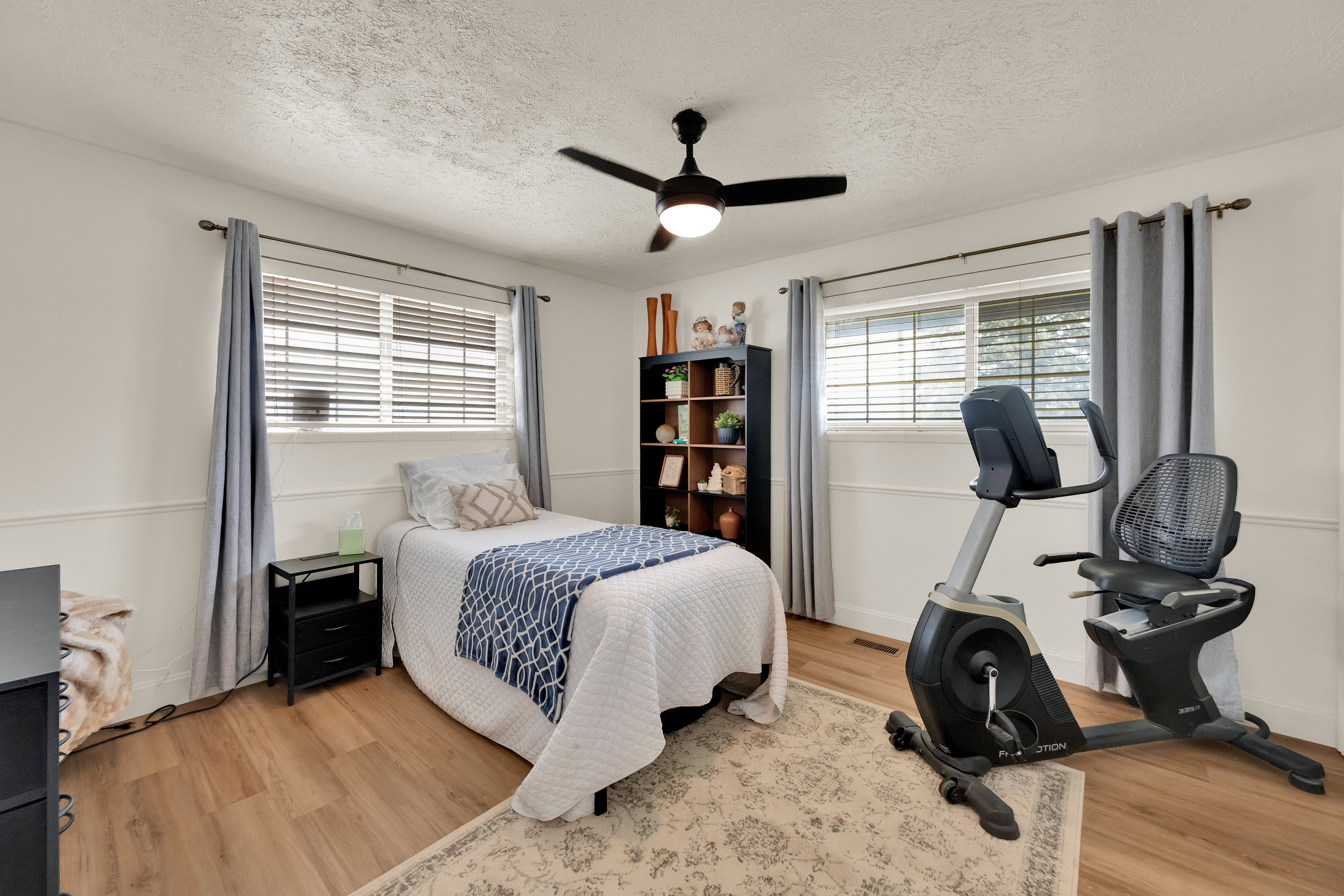 Bright room featuring two large windows with blinds, wood-finish flooring, and a ceiling fan