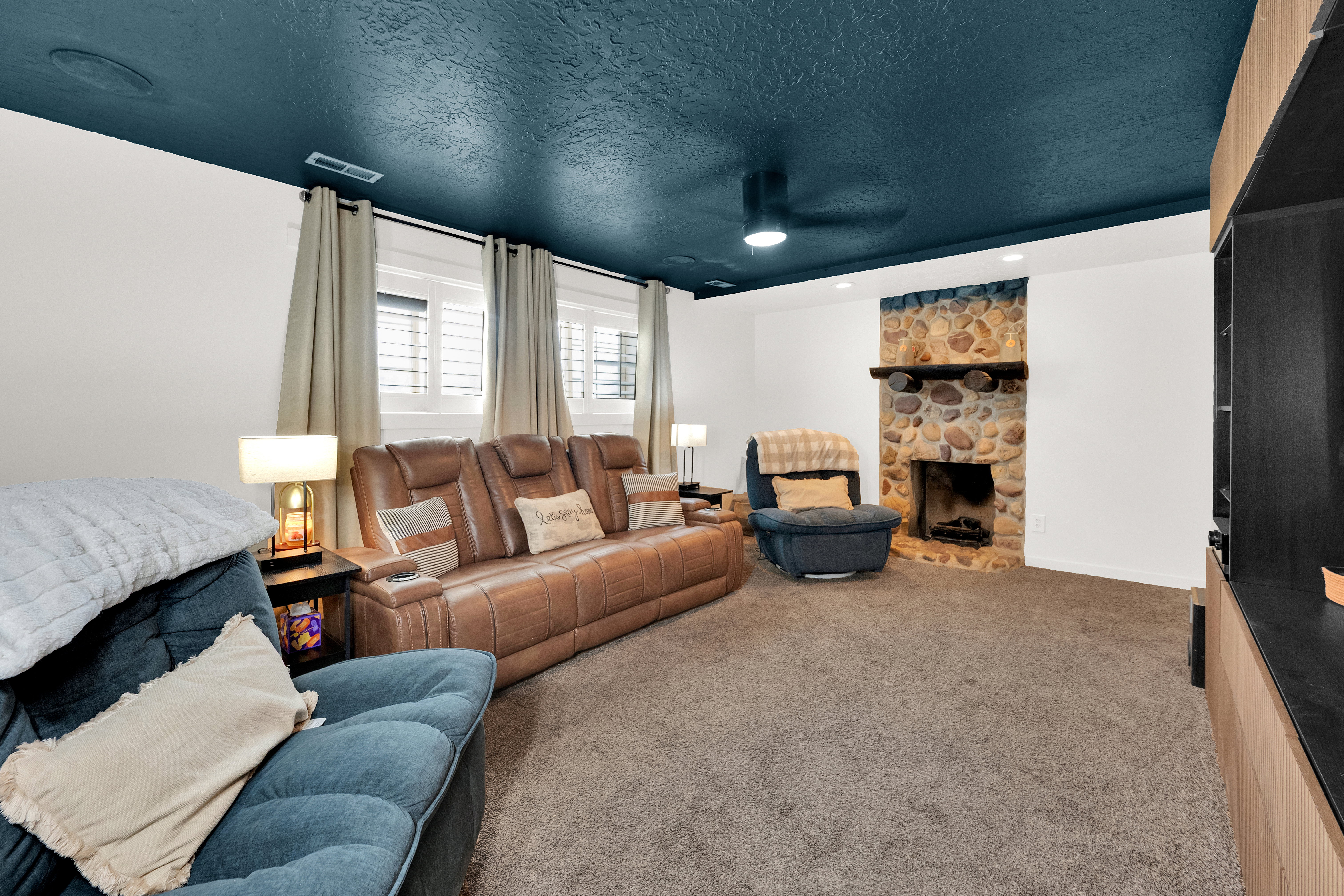 Spacious room featuring a stone-faced fireplace with a wood mantle, a contrasting dark ceiling, recessed lighting, and multiple windows with blinds