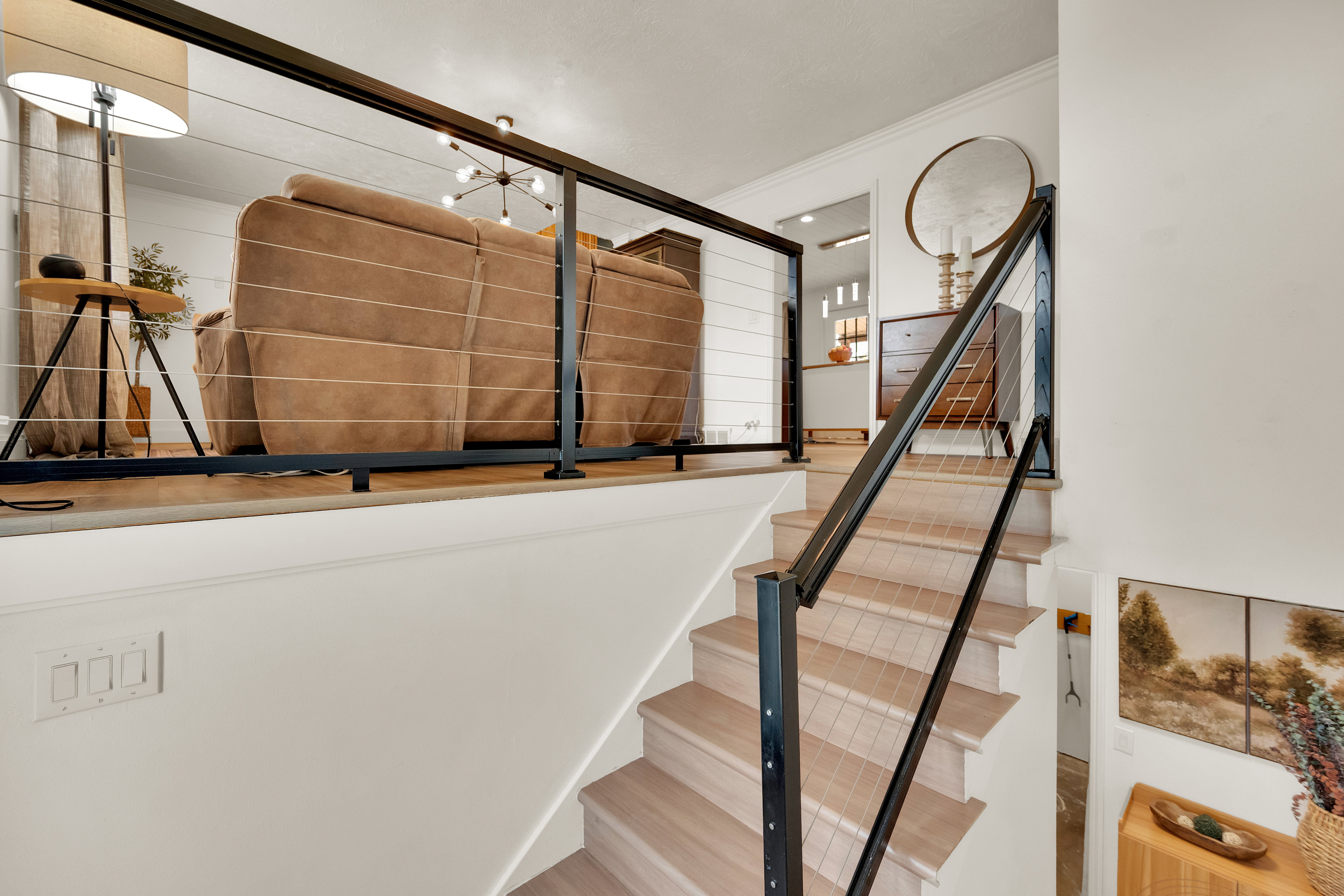 Split-level interior featuring light wood-finish flooring, a modern cable railing system, and neutral wall tones