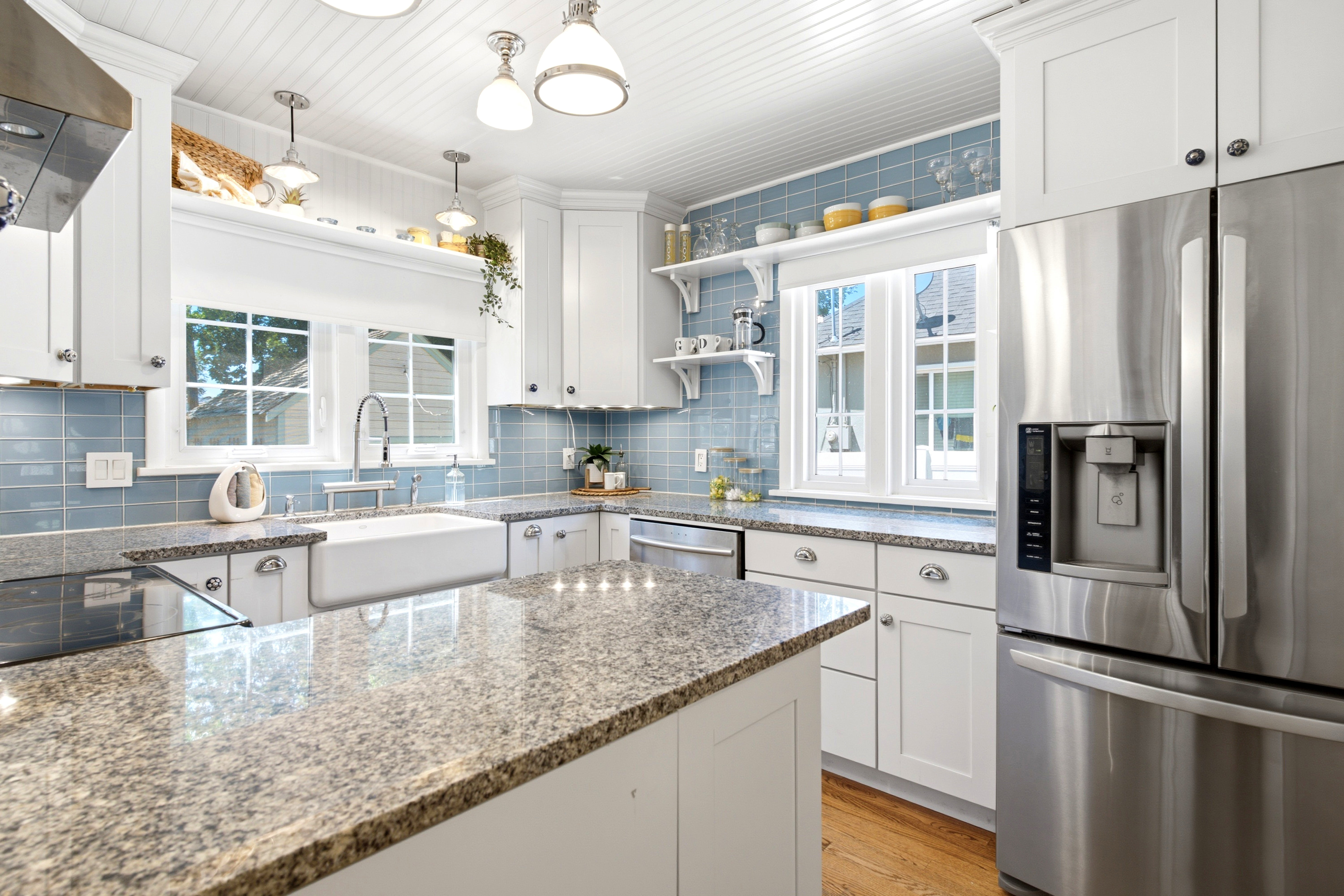 White shaker style cabinetry, granite countertops, stainless steel appliances, a farmhouse sink, and subway tile backsplash