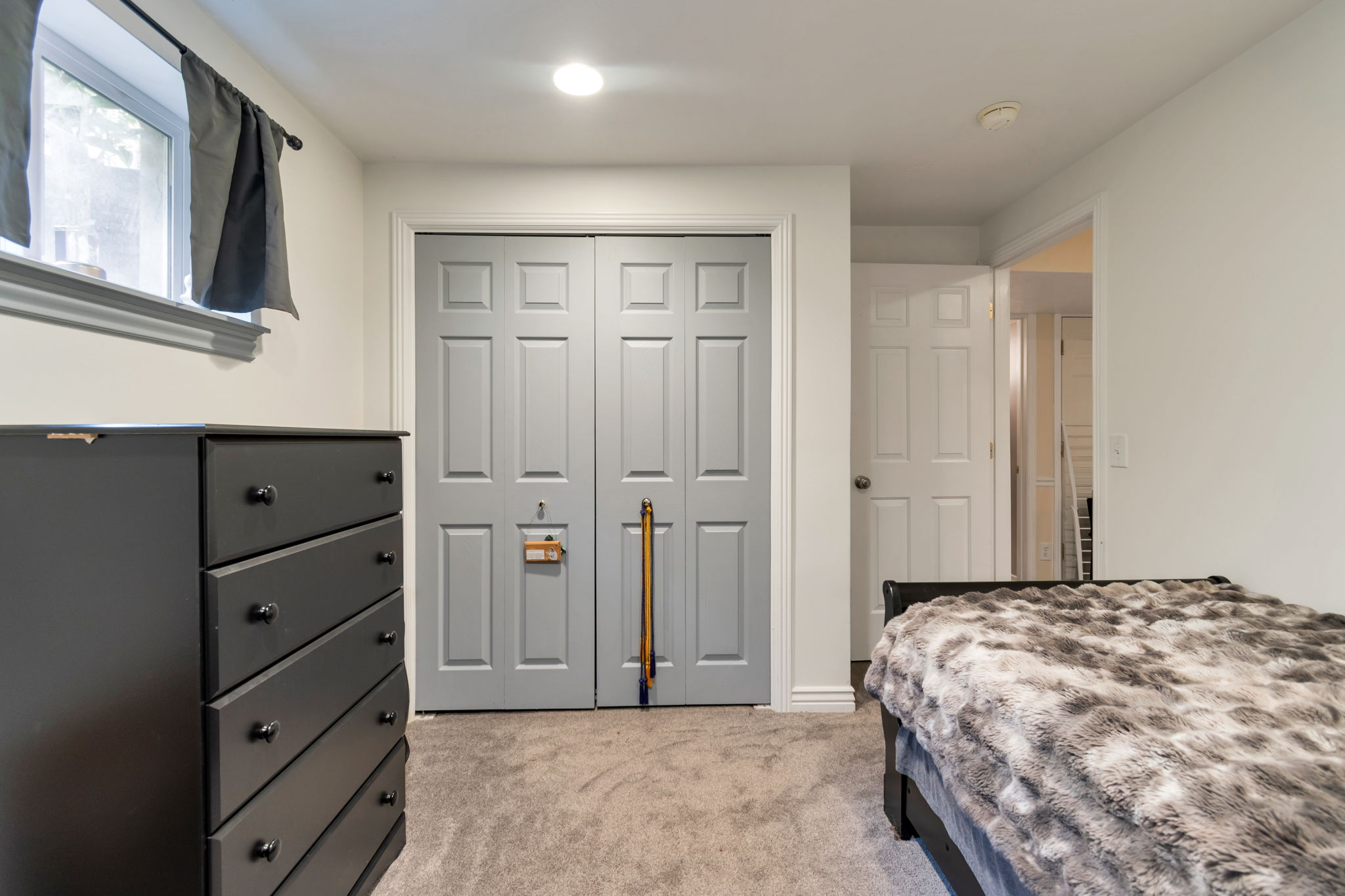 Room featuring light gray paneled closet doors, neutral tone carpeting, and a single window with white trim