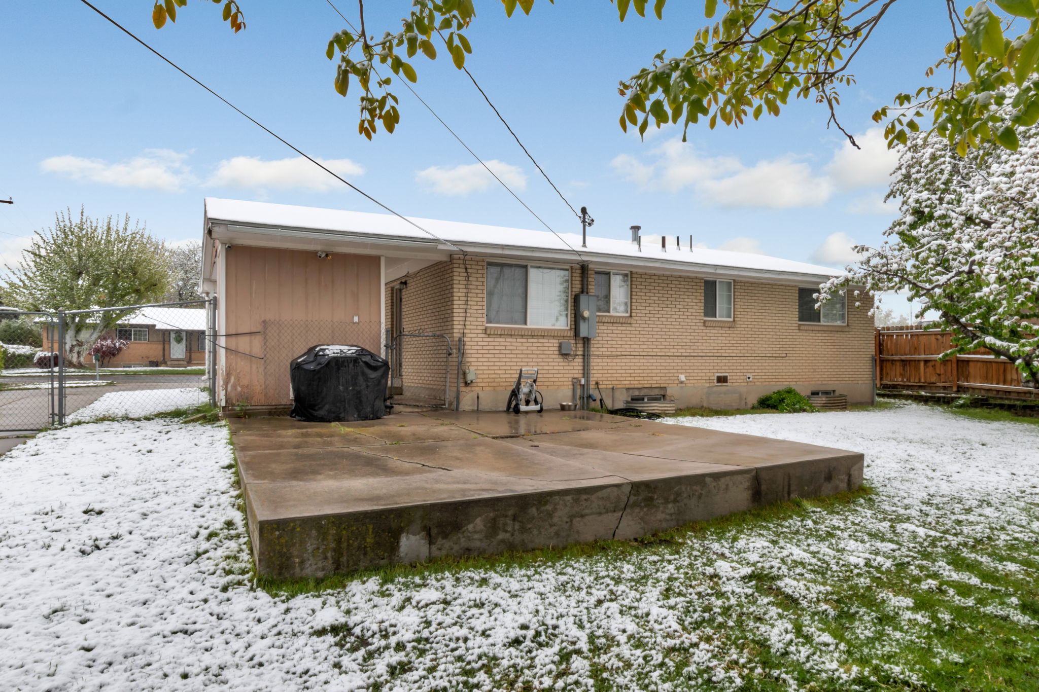 Rear exterior featuring a concrete patio, brick siding, an attached covered structure, and a partial wood privacy fence