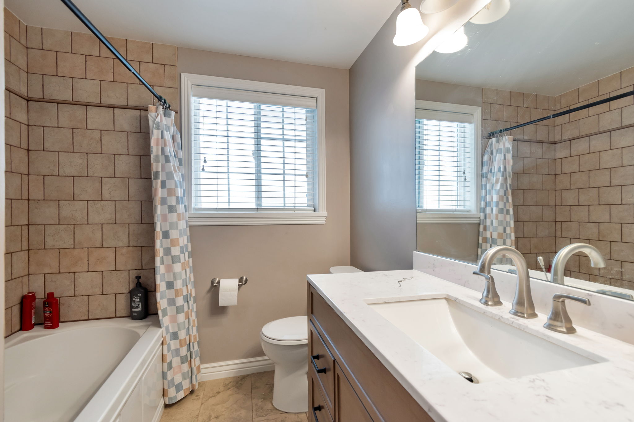 Bathroom featuring a white vanity with an integrated sink, brushed nickel fixtures, a large mirror, and a window with blinds